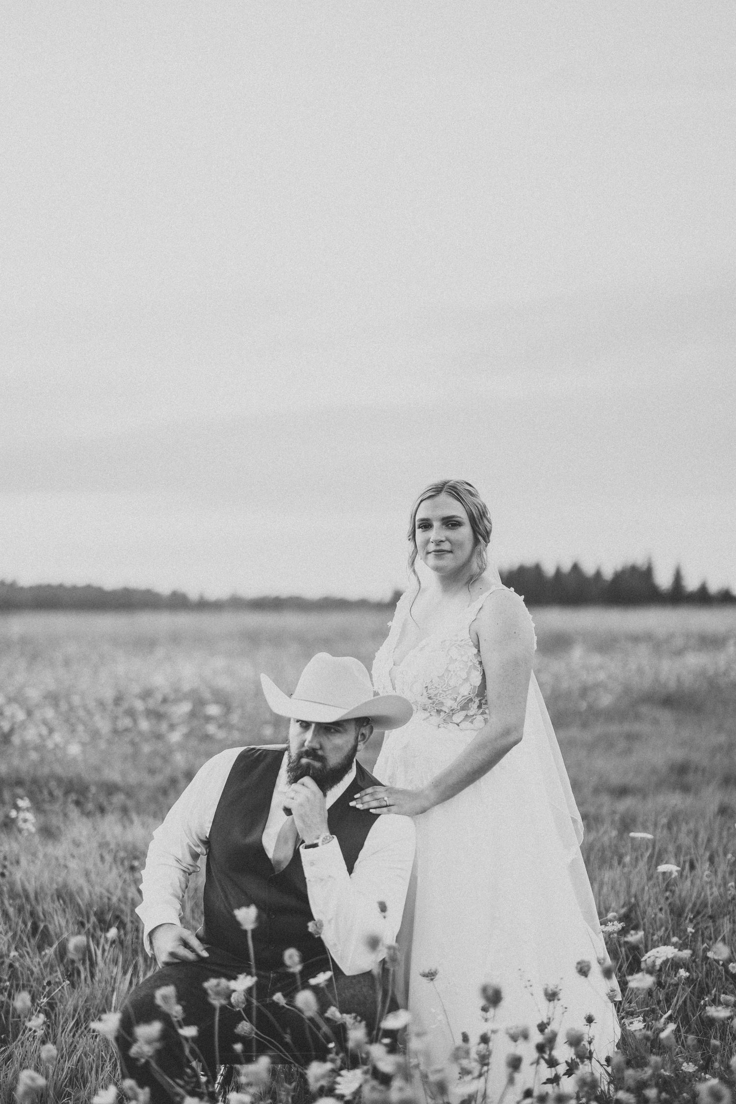Black and white portrait of couple in wildflower field with dramatic sky.