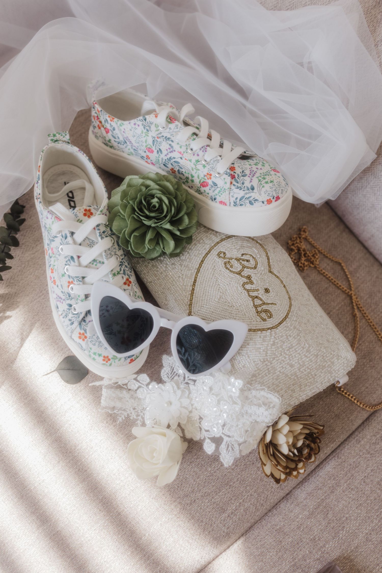 Floral print sneakers with heart sunglasses and delicate accessories arranged on light fabric.