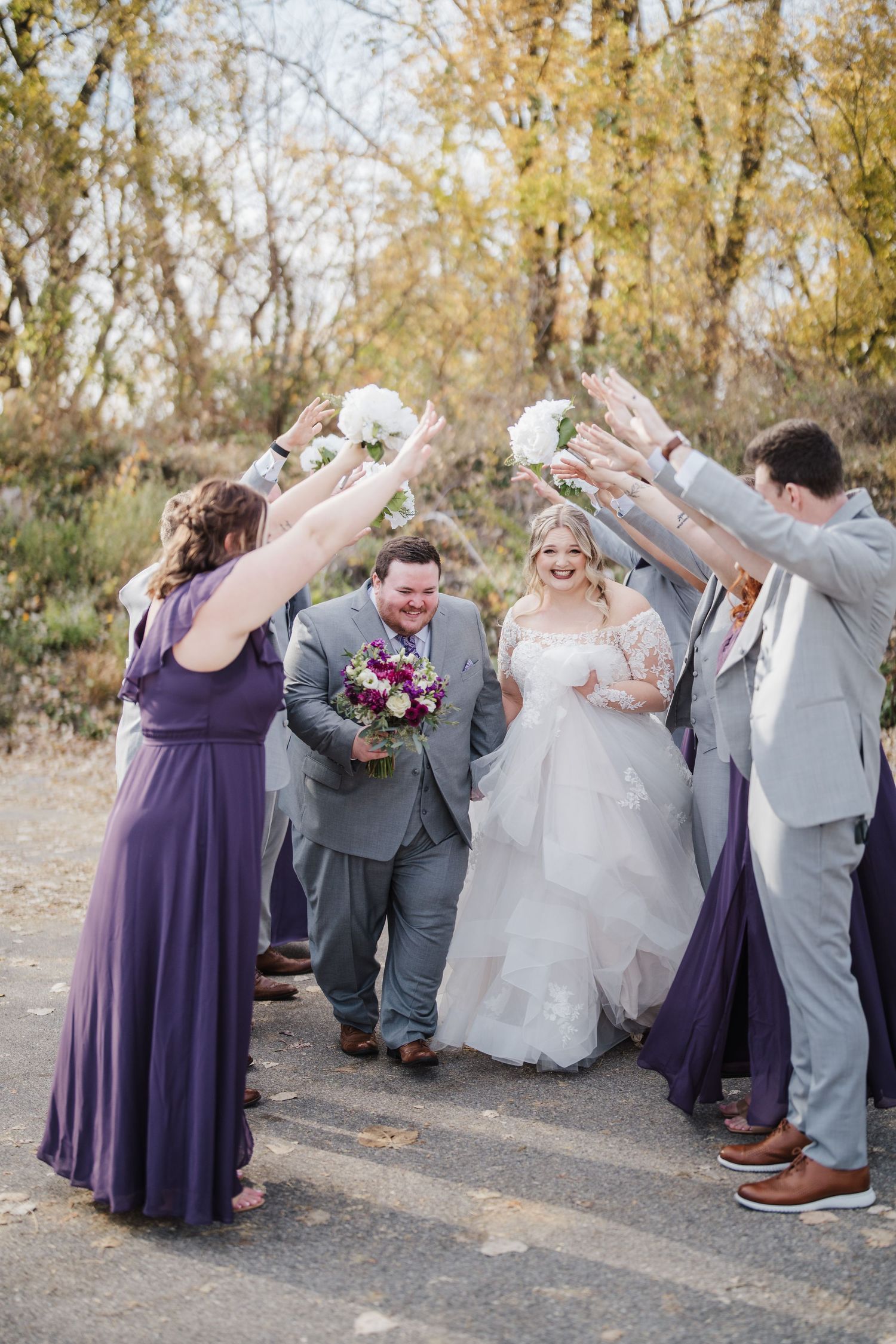 Wedding party creates a tunnel arch for the newlyweds during an autumn outdoor celebration.
