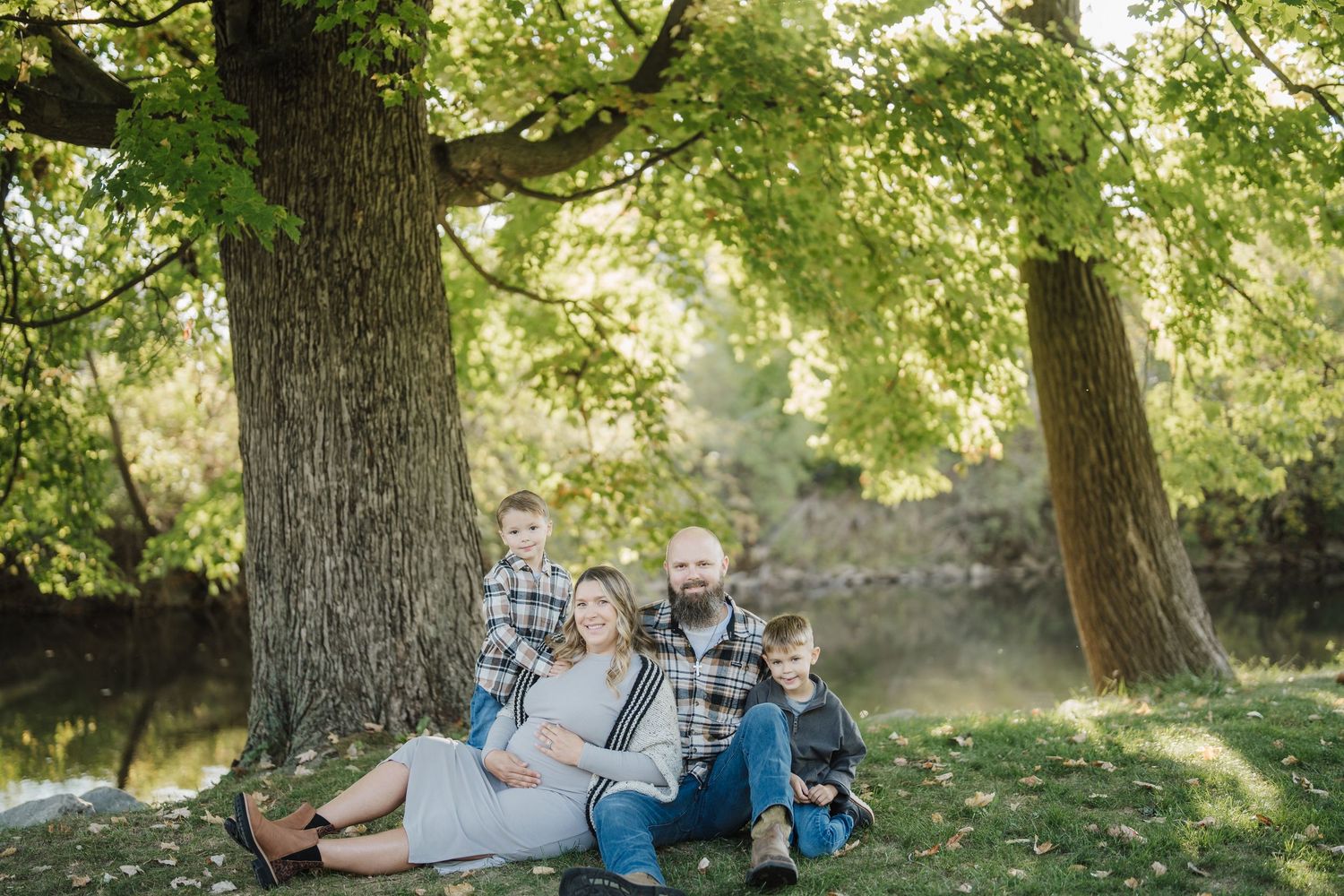 A family relaxes together on a blanket under a large tree in a sunlit park during a summer afternoon.