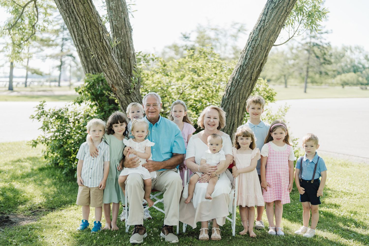 A group in coordinated pastel outfits poses together outdoors on a sunny day near trees.
