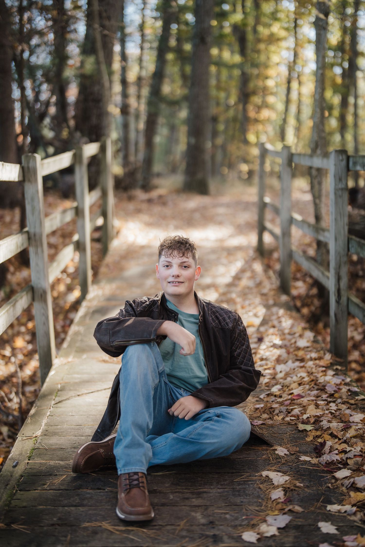A person relaxes on a wooden boardwalk path surrounded by autumn leaves and pine trees in a forest setting.