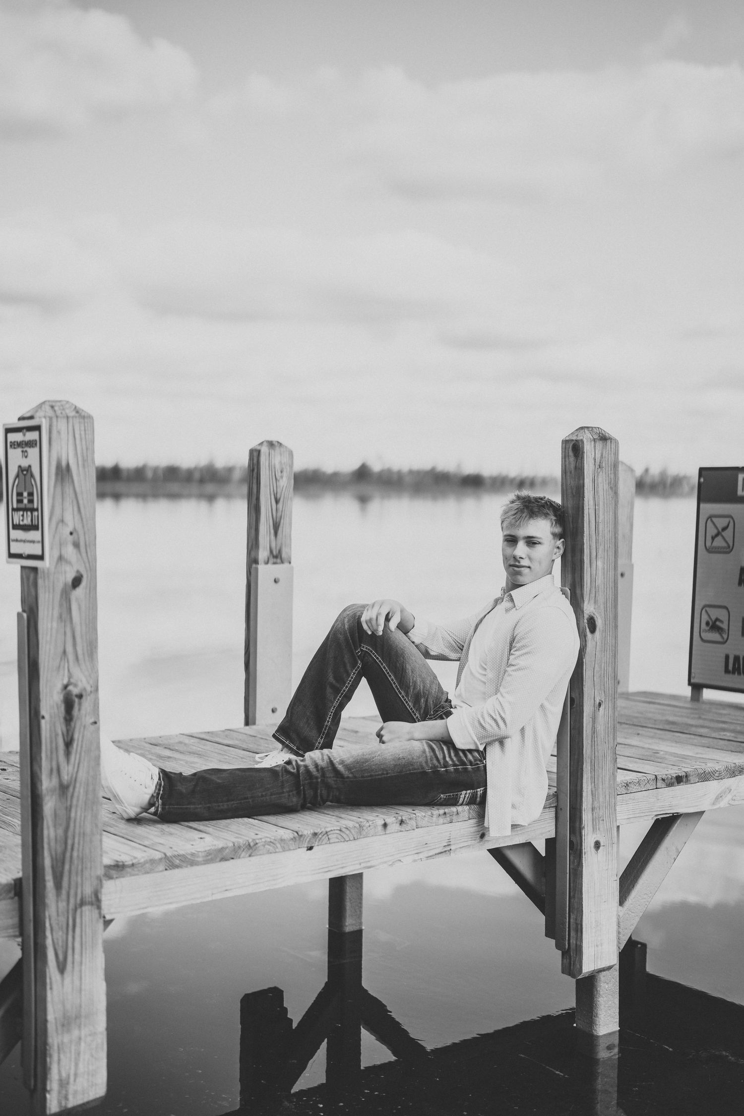 A person relaxes on a wooden pier overlooking a tranquil lake in black and white photography.