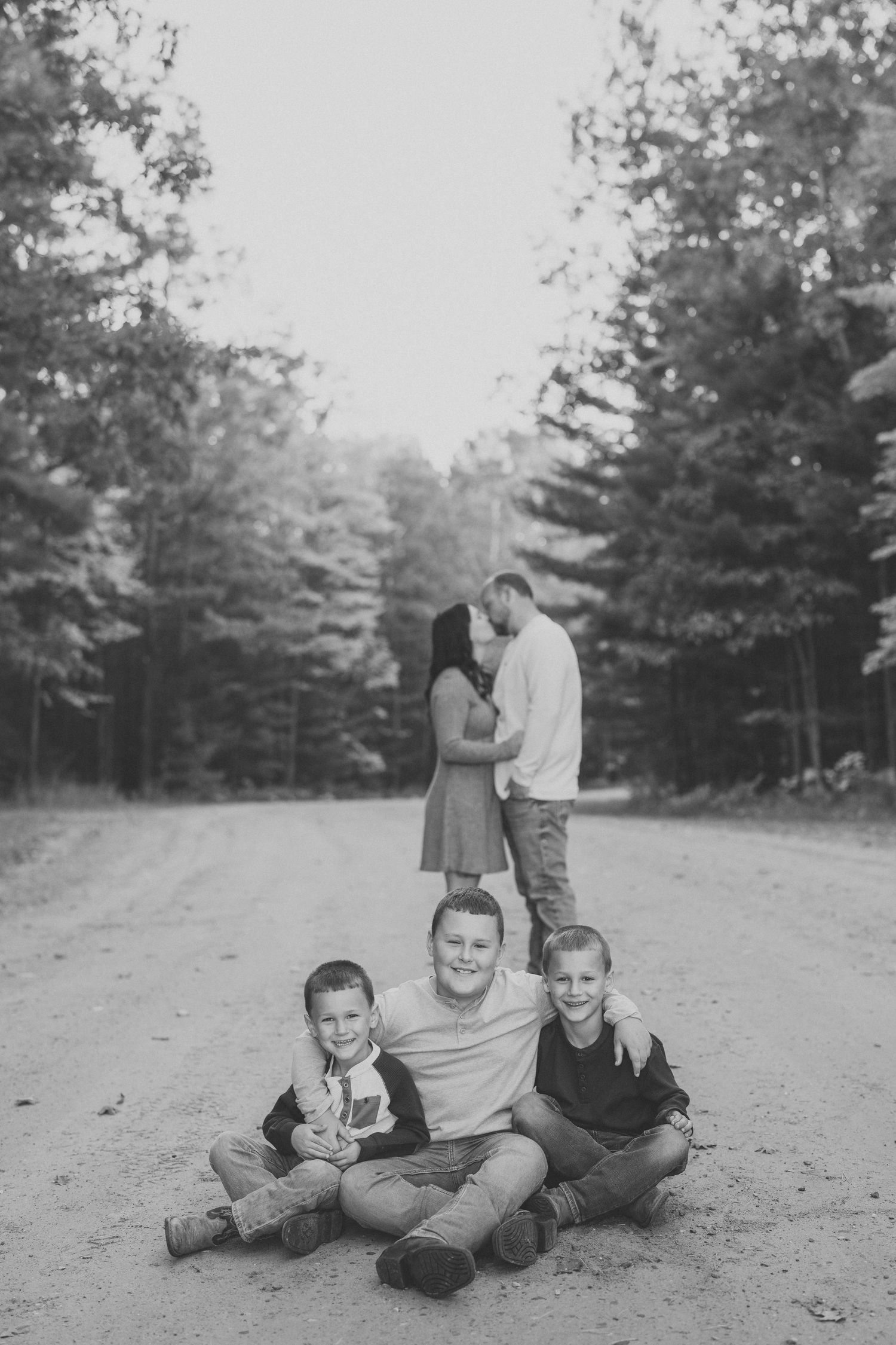 A black and white photo series showing a couple lying on the ground in a wooded area, captured in four romantic poses.