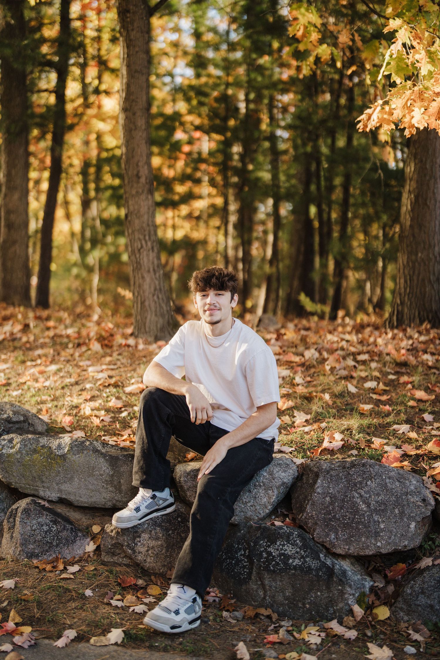Casual outdoor portrait on rocky terrain with fall foliage and trees in background.