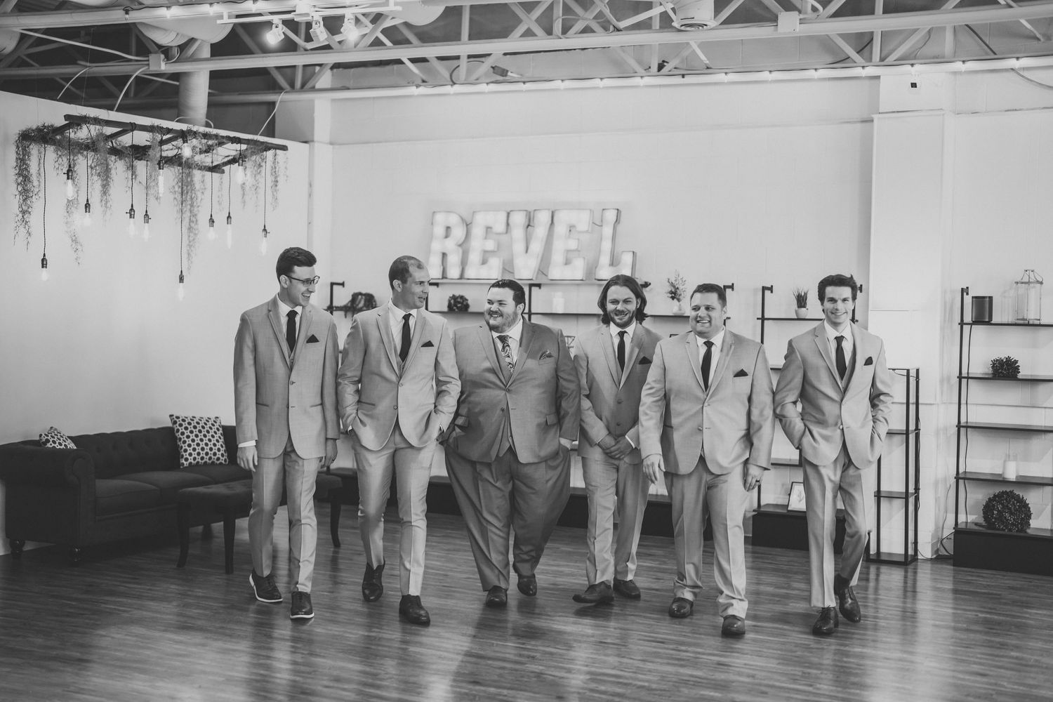 A vintage black and white photo shows groomsmen in matching suits walking in formation at a wedding venue.