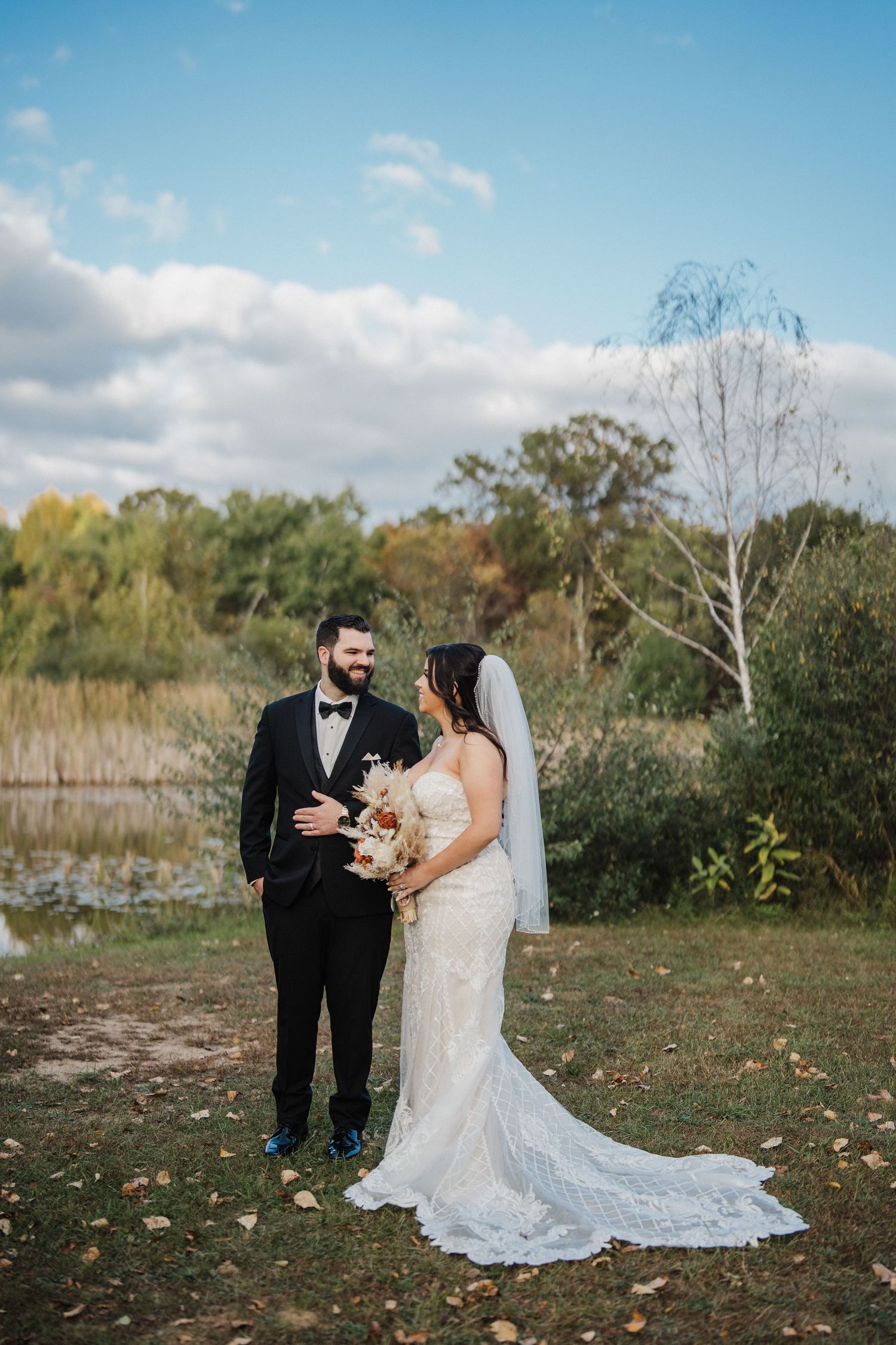 A couple in wedding attire shares a joyful moment together in a scenic outdoor setting with autumn foliage.