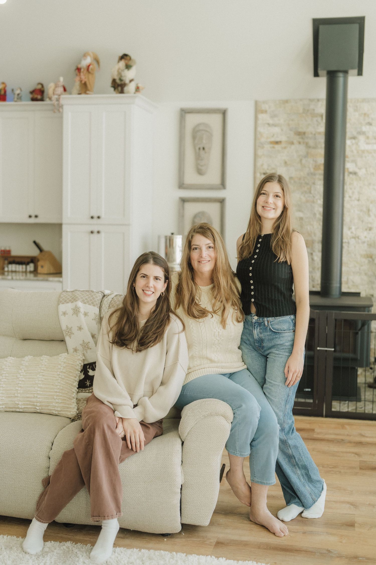 Group of friends lounging together on beige couch in bright modern living room with hardwood floors and stone wall.