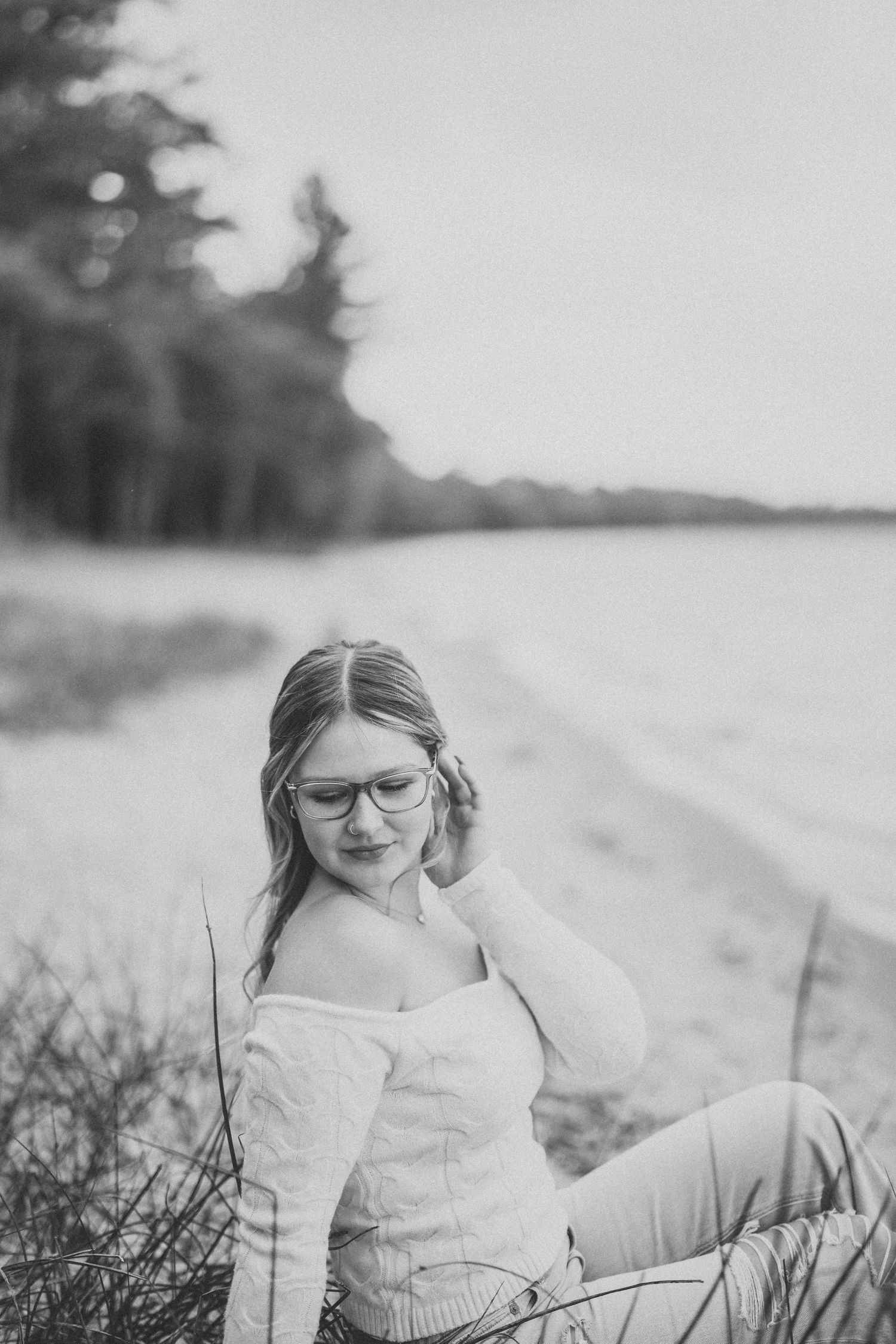 Black and white portrait of a young person with glasses sitting in a grassy field on a sunny day.