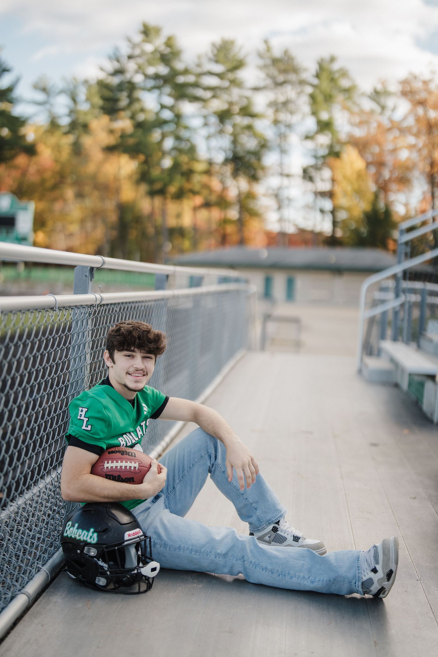 A young football player in a green jersey lying on bleachers with a football during a fall photo session.