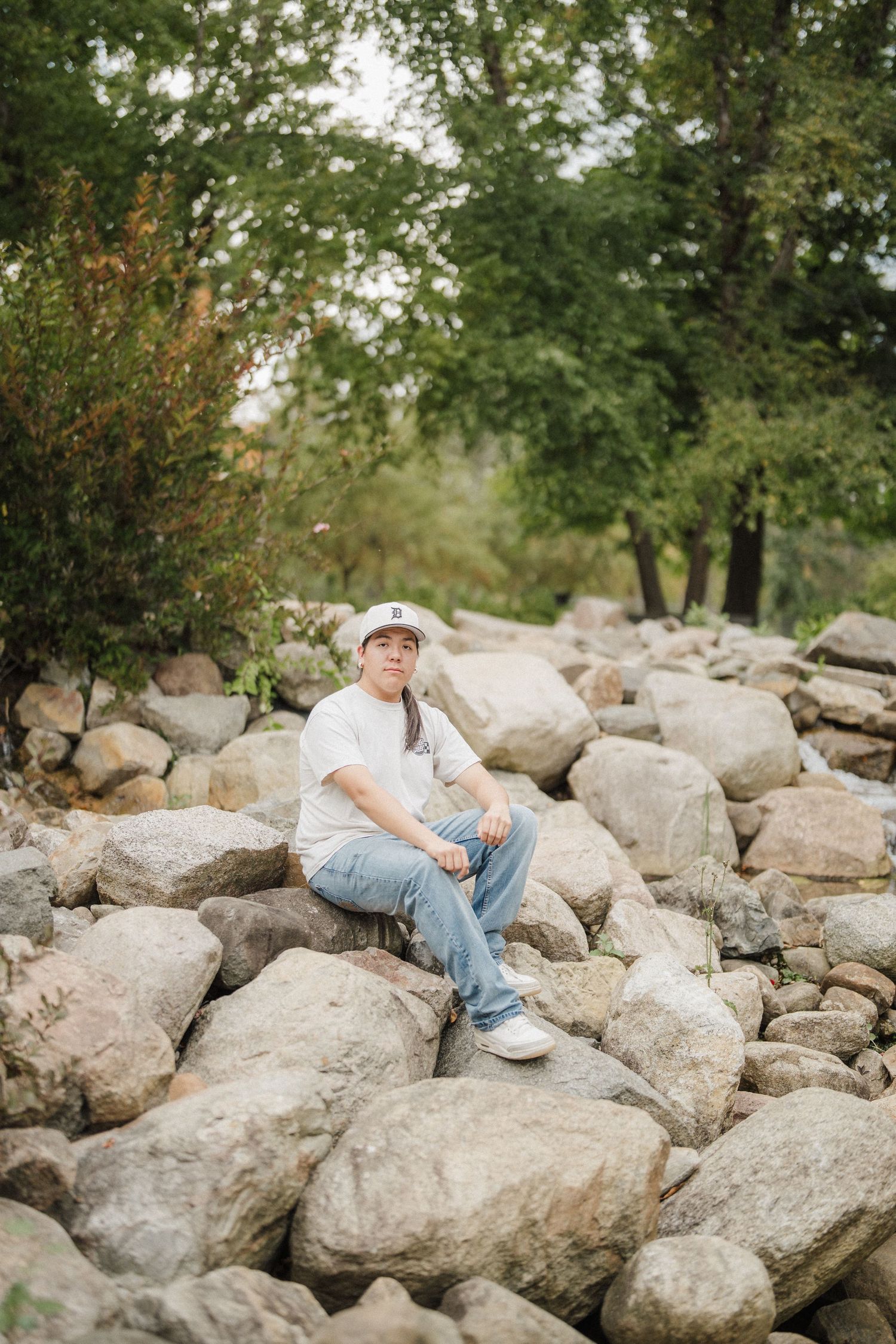 Person in casual attire sits relaxed on large rocks in a natural outdoor setting.