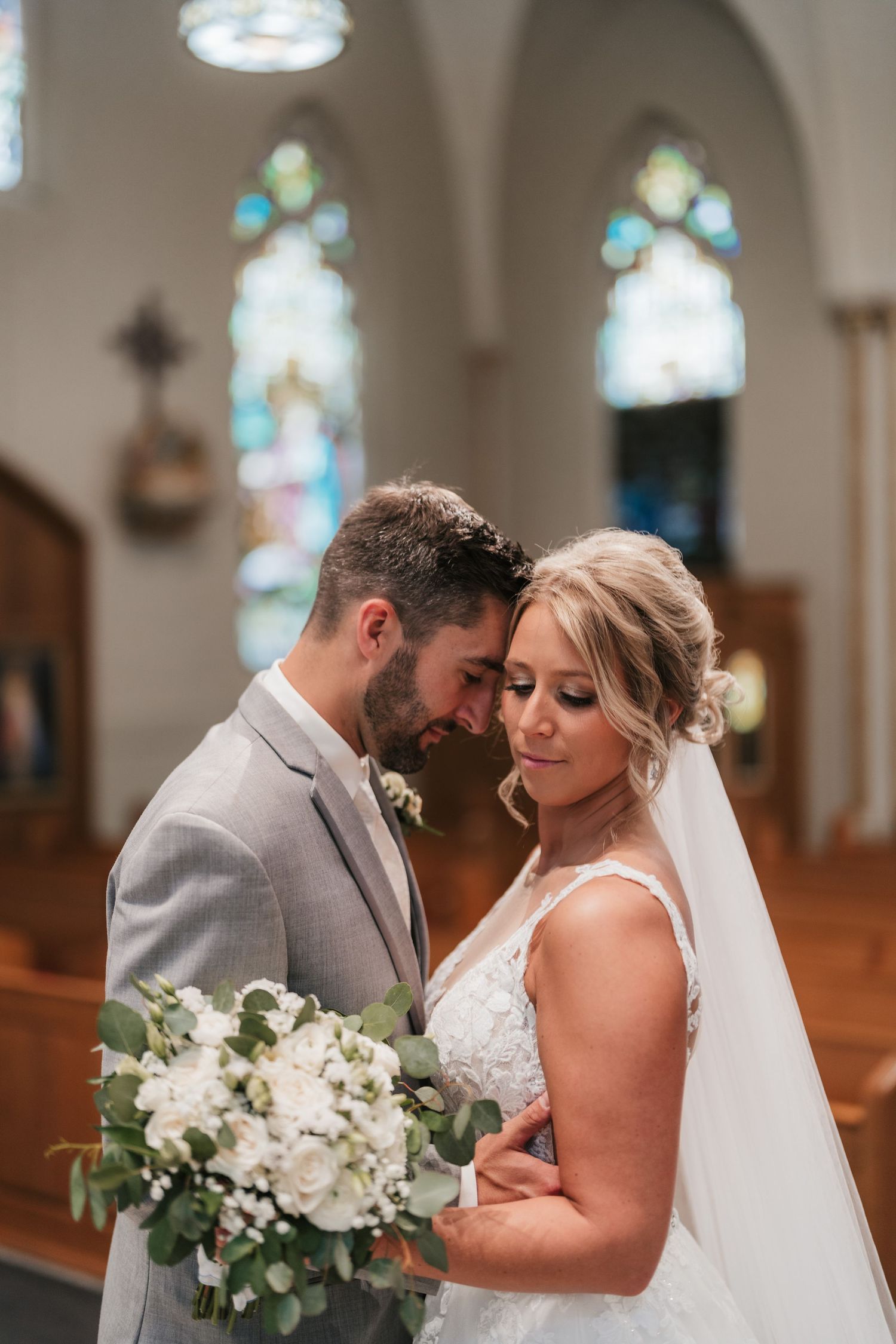 Intimate moment captured between newlyweds inside church with stained glass windows.