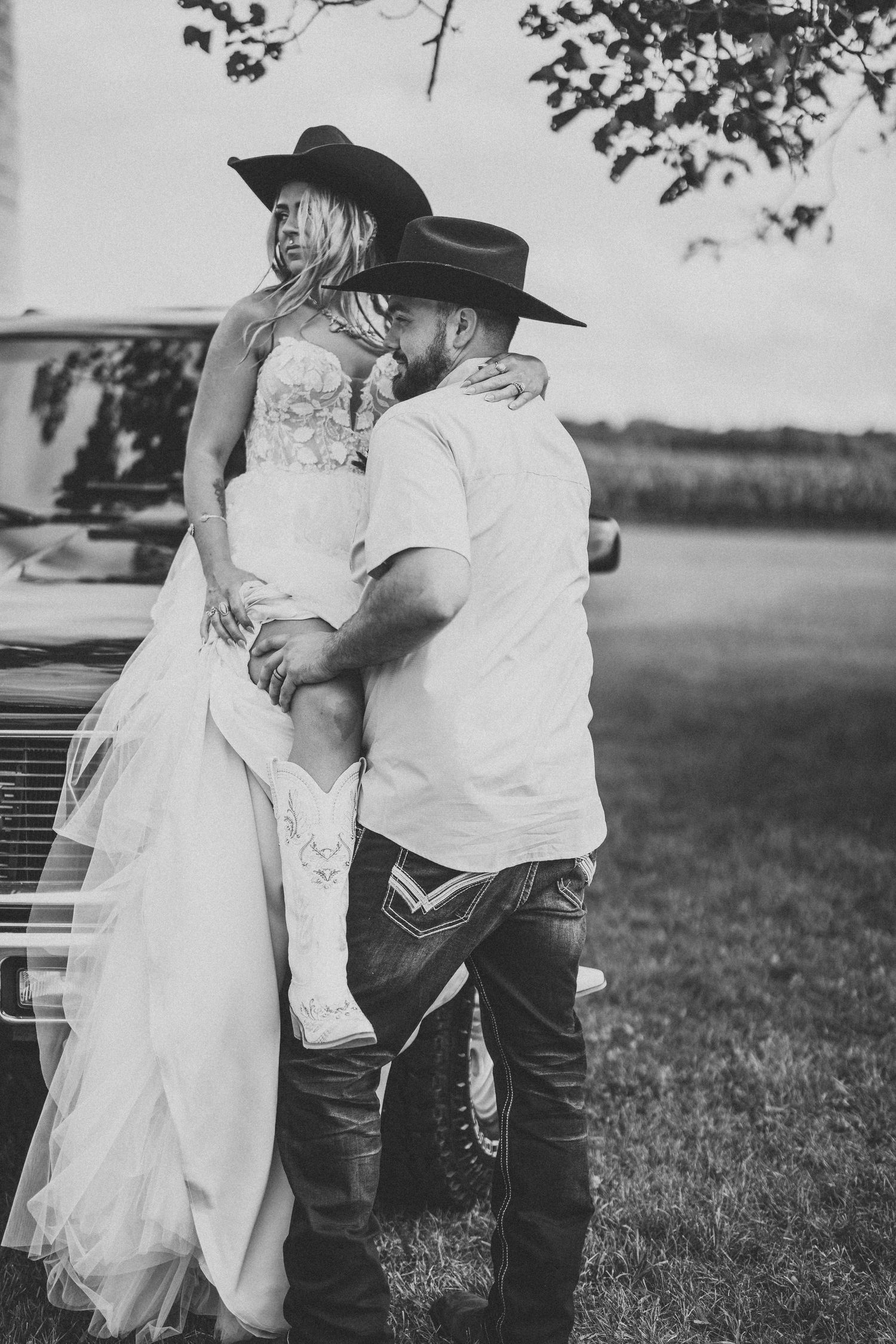 Black and white photo of western-styled couple in wedding attire by vintage truck.