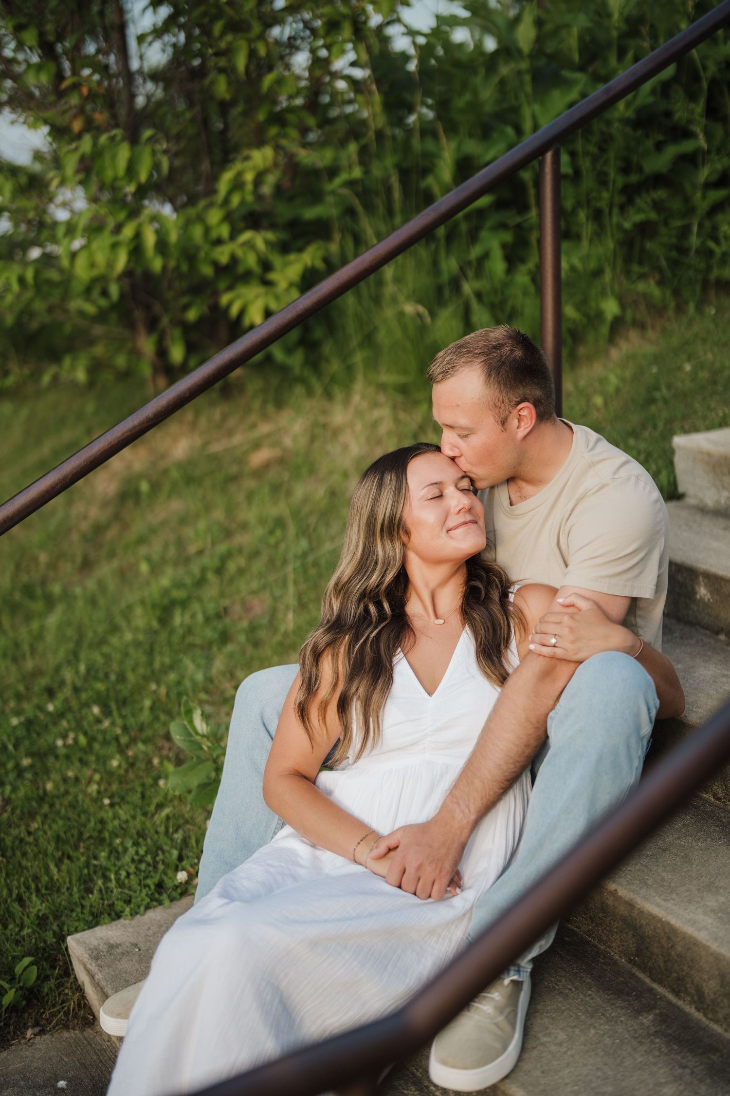 A couple in white and light colored clothing share intimate moments while sitting on outdoor steps.