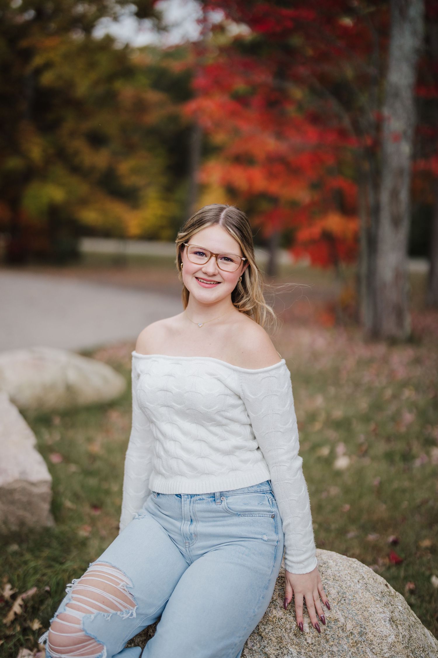 A casual autumn portrait featuring light denim and white sweater against vibrant red fall foliage.