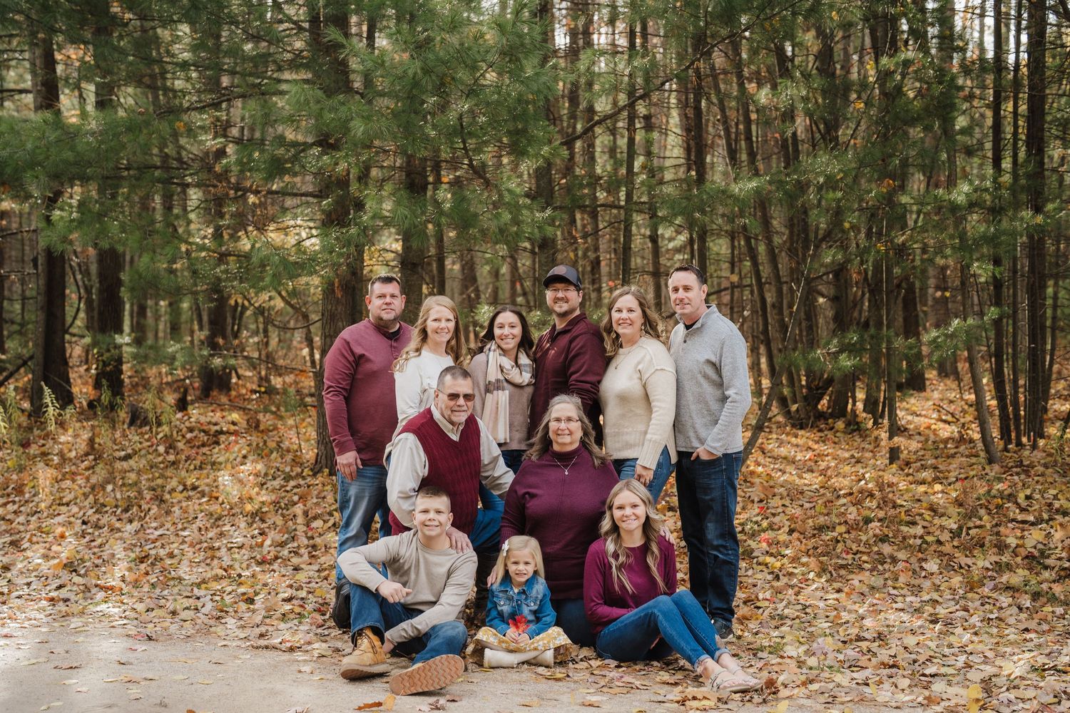 A group poses together on a leaf-covered path in an autumn forest setting during a fall photo session.