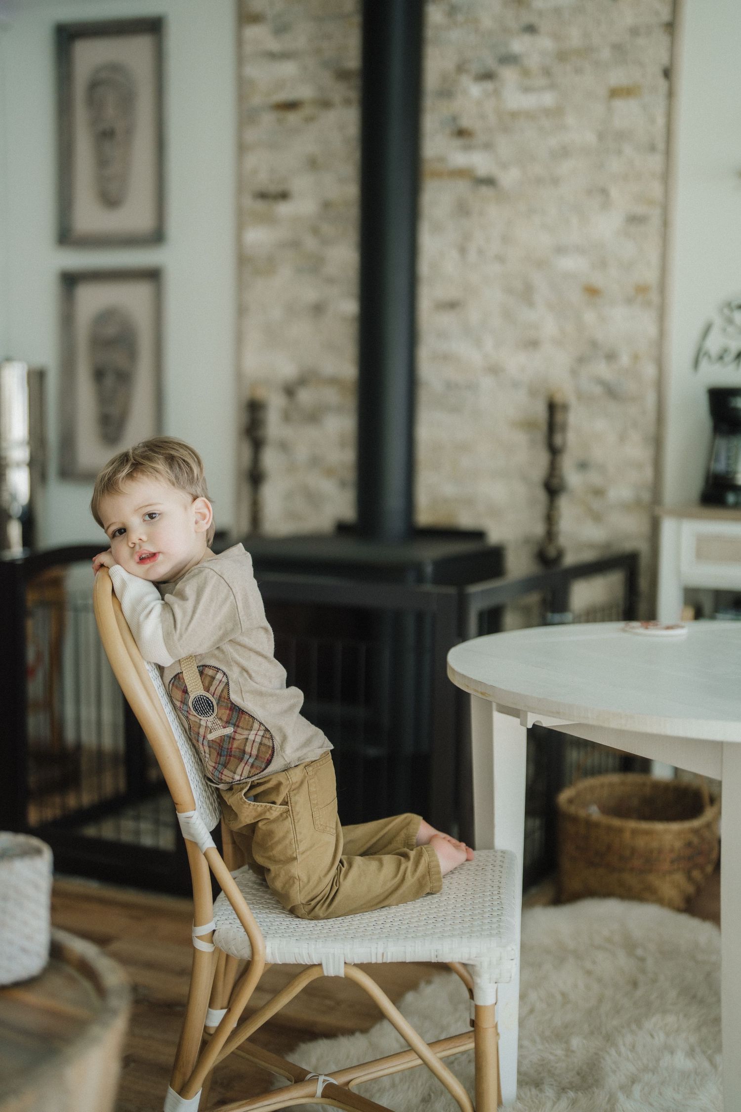 A young child sits in various poses on a wooden chair against a rustic brick wall interior.