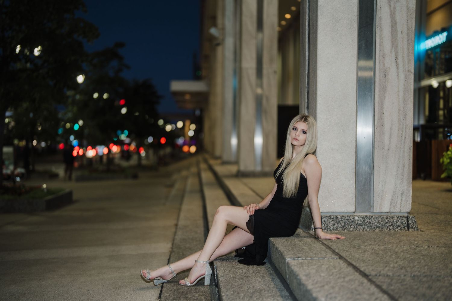 A woman in a black dress poses for a series of photos against concrete columns at night.
