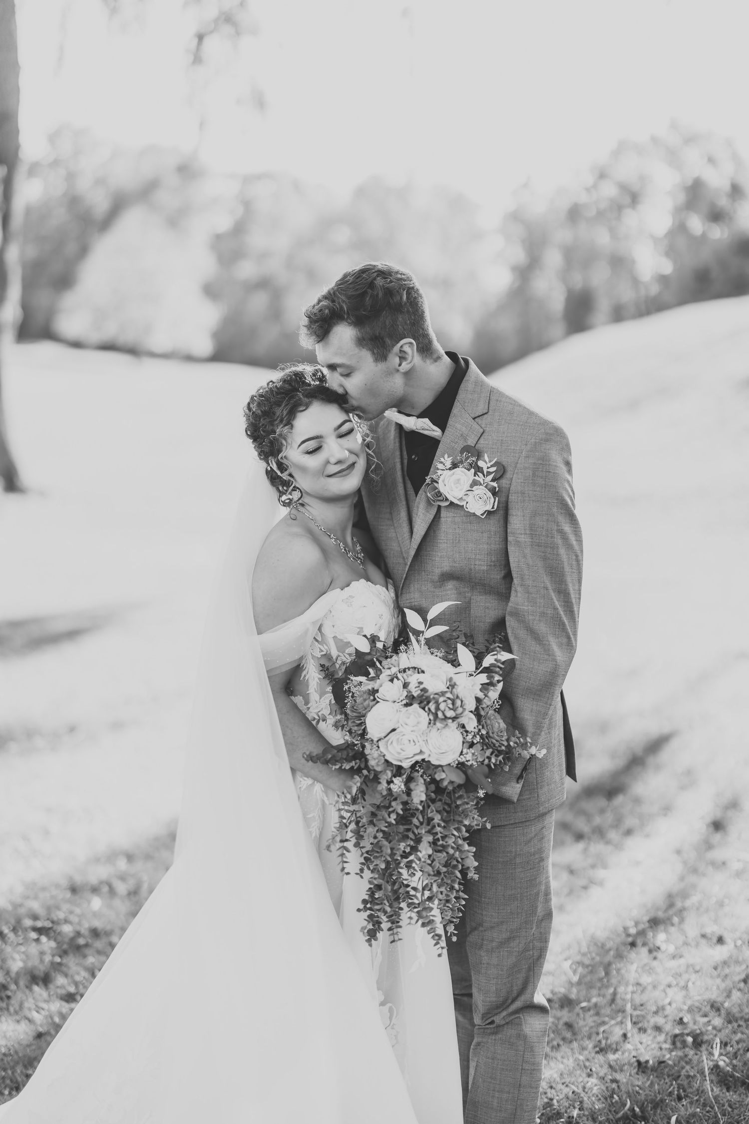 Black and white wedding portrait of couple with bridal bouquet in outdoor setting.