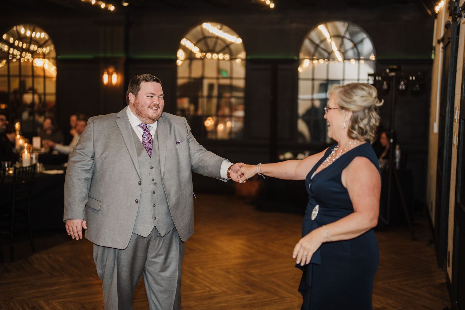 Wedding reception dance features couple moving across hardwood floor under ambient lighting.