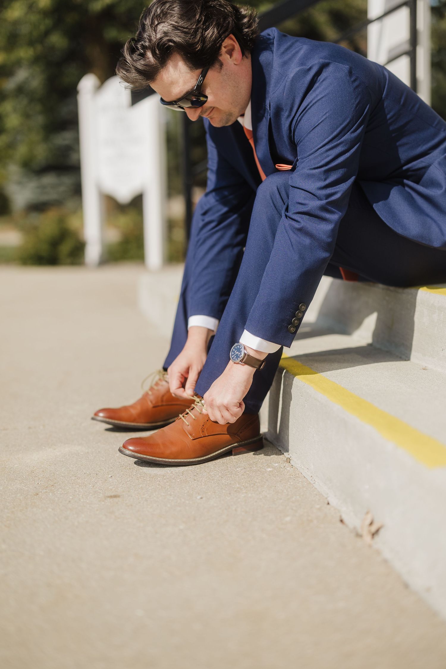 Close-up view of brown leather dress shoes being tied on concrete steps.