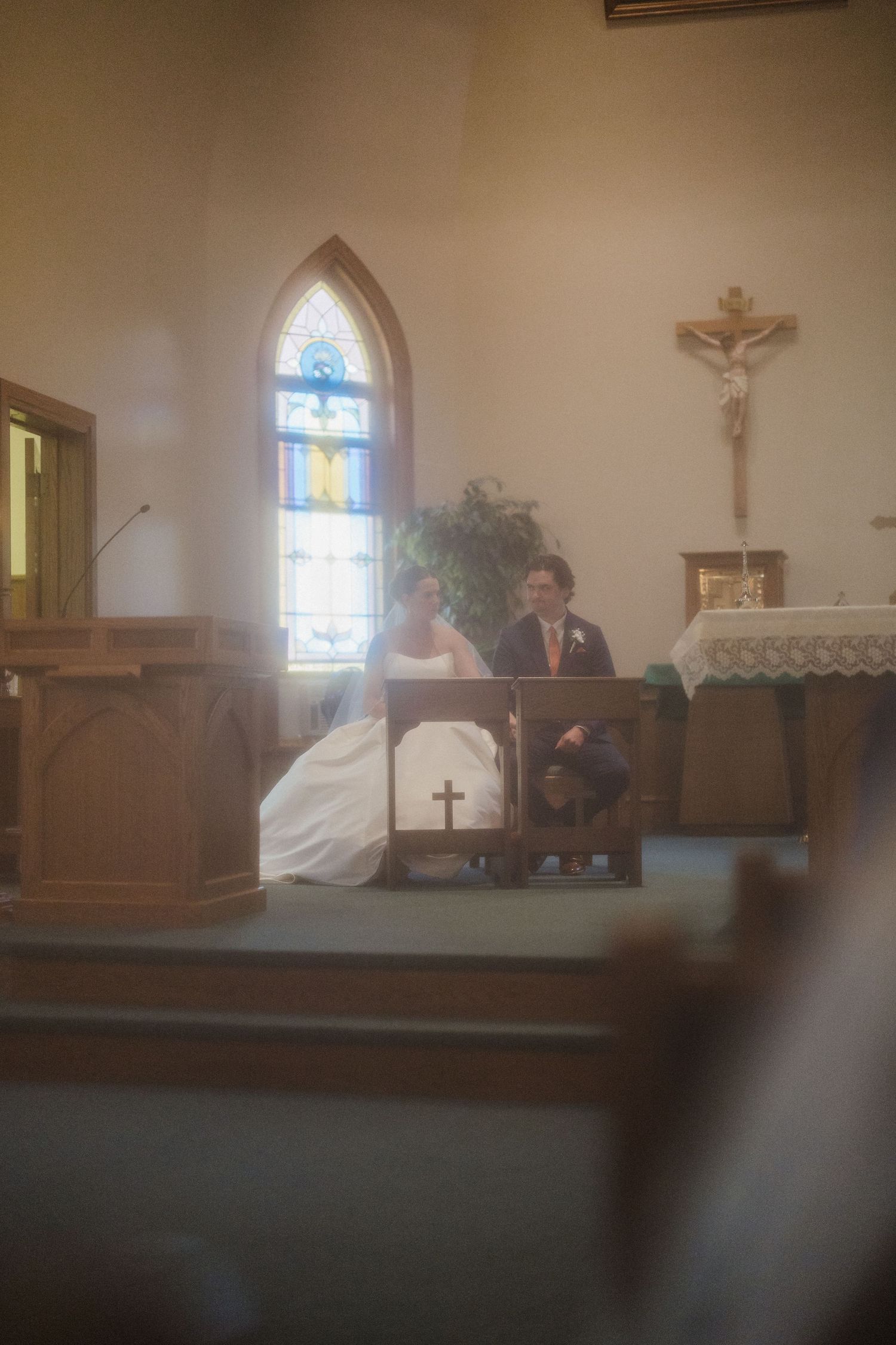 A sunlit church interior with stained glass windows and wooden pews during a wedding ceremony.