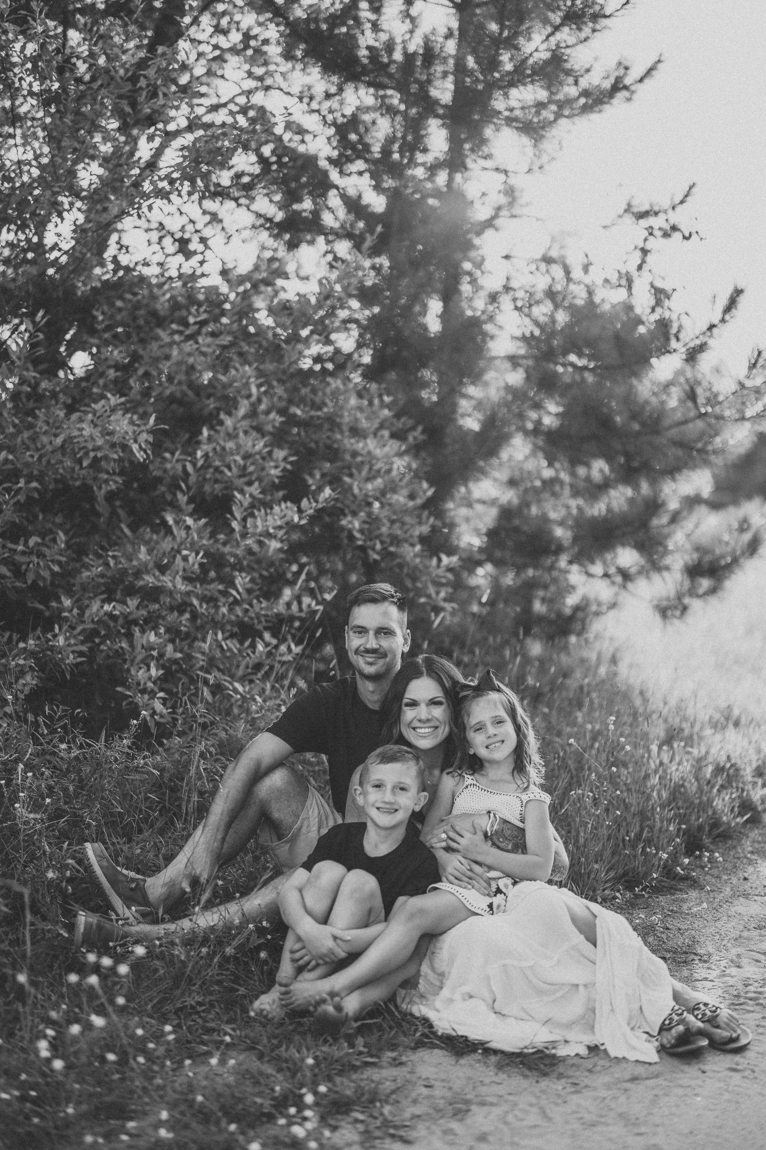 Black and white portrait of a family relaxing together on a hillside with trees in the background.