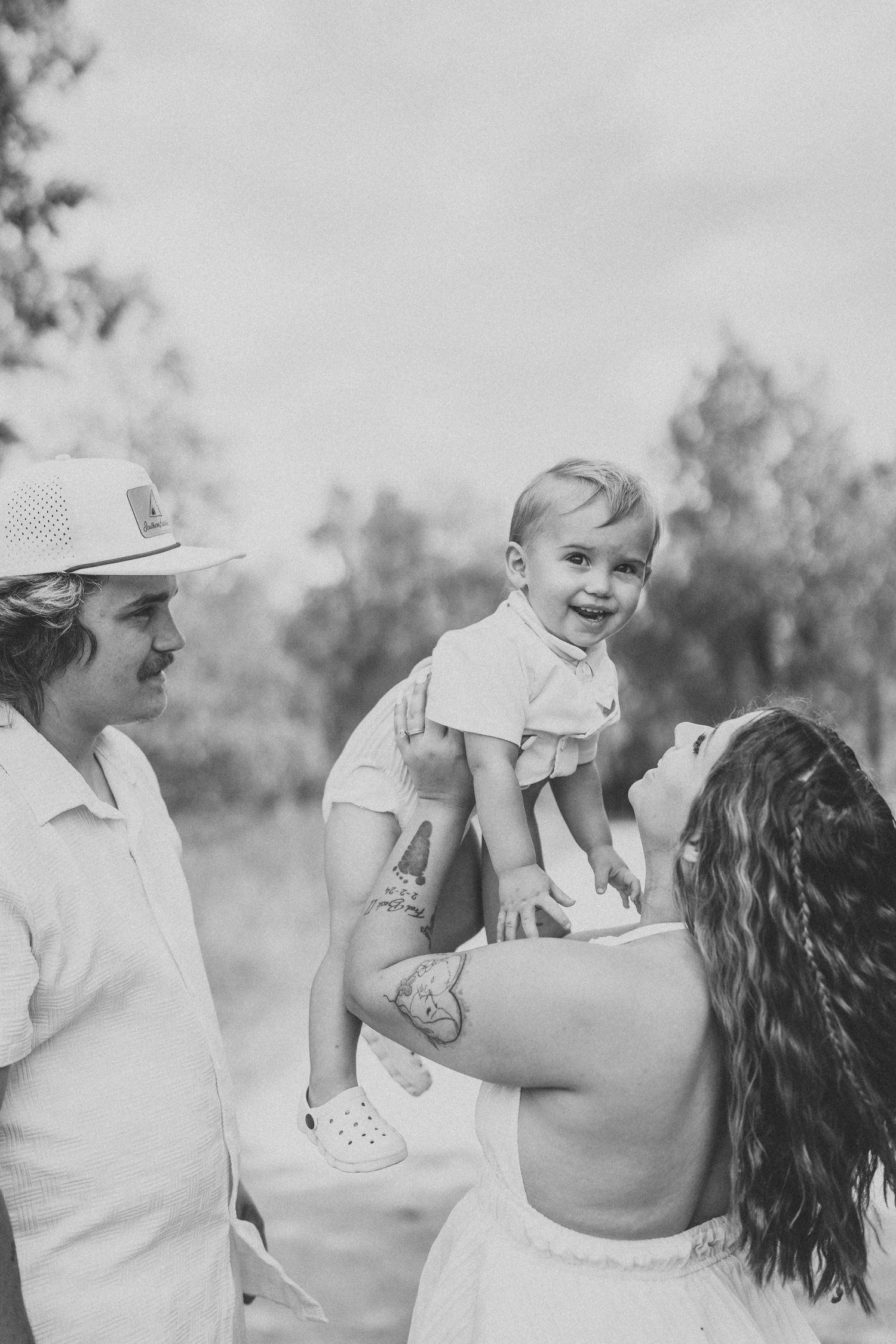 A joyful family moment captured in black and white as they share loving embraces outdoors in a natural setting.