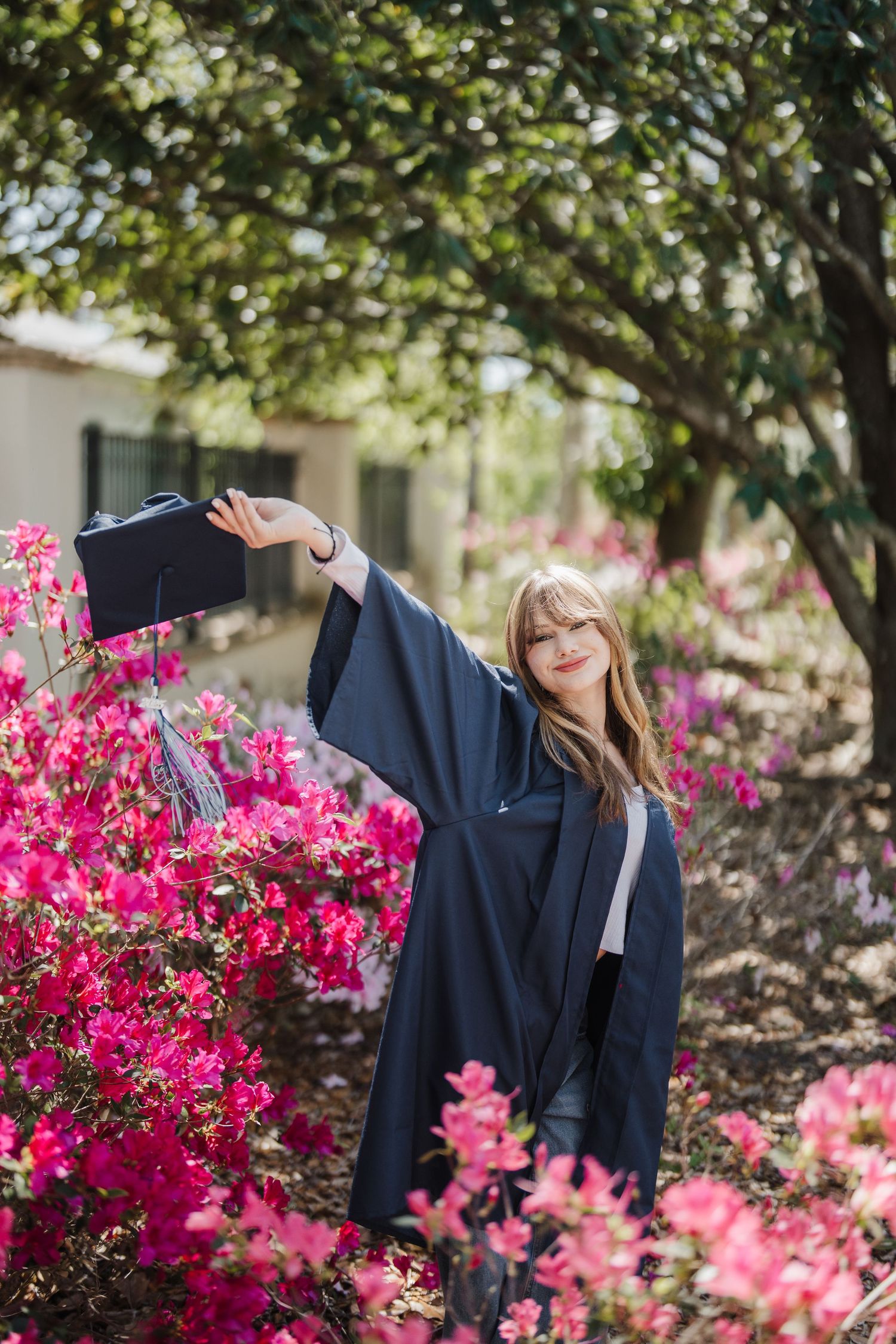 A graduation gown displayed against vibrant pink azalea bushes in bloom creating a colorful spring scene.