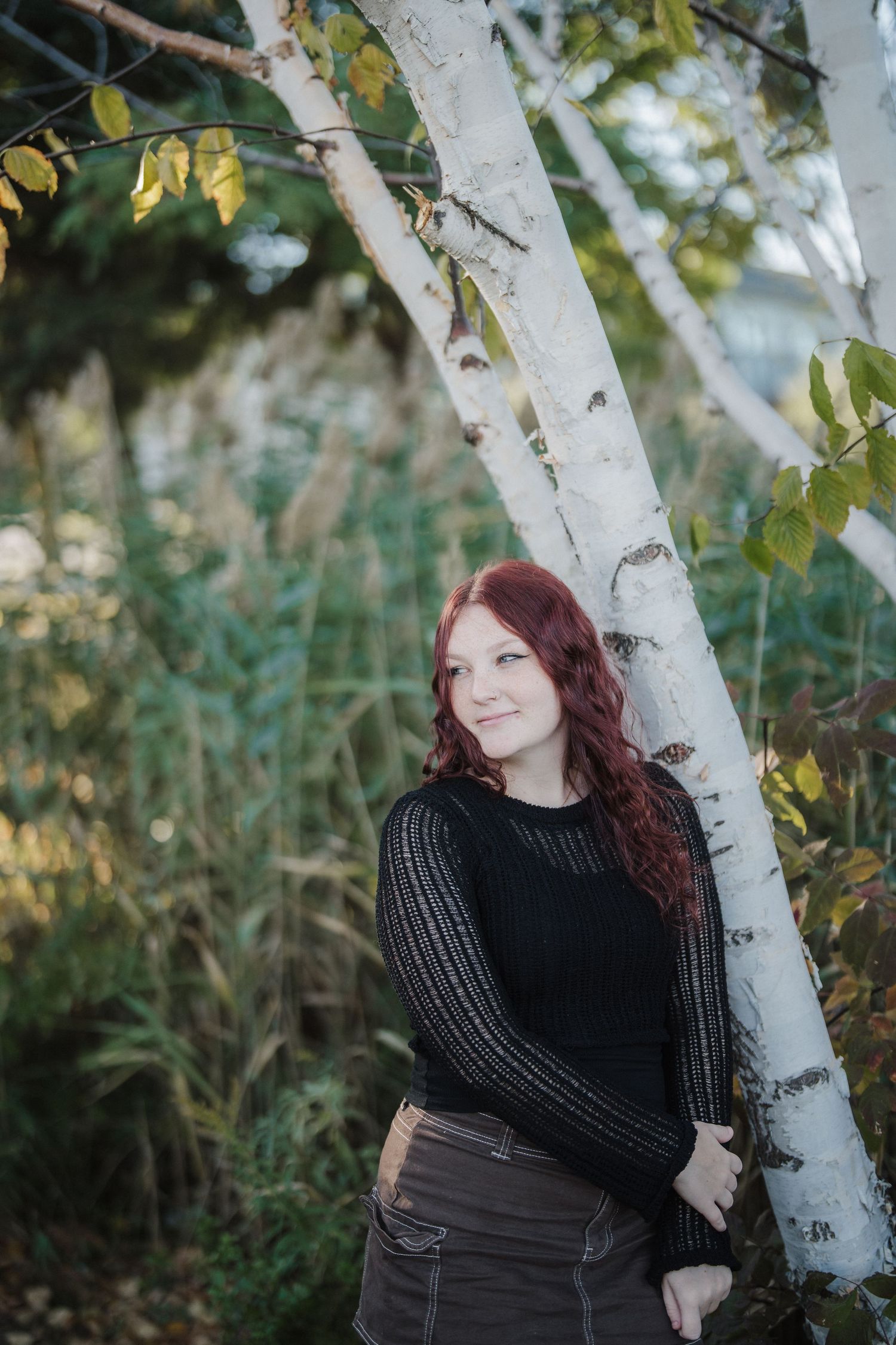Outdoor portrait session against white birch trees with fall foliage in the background.