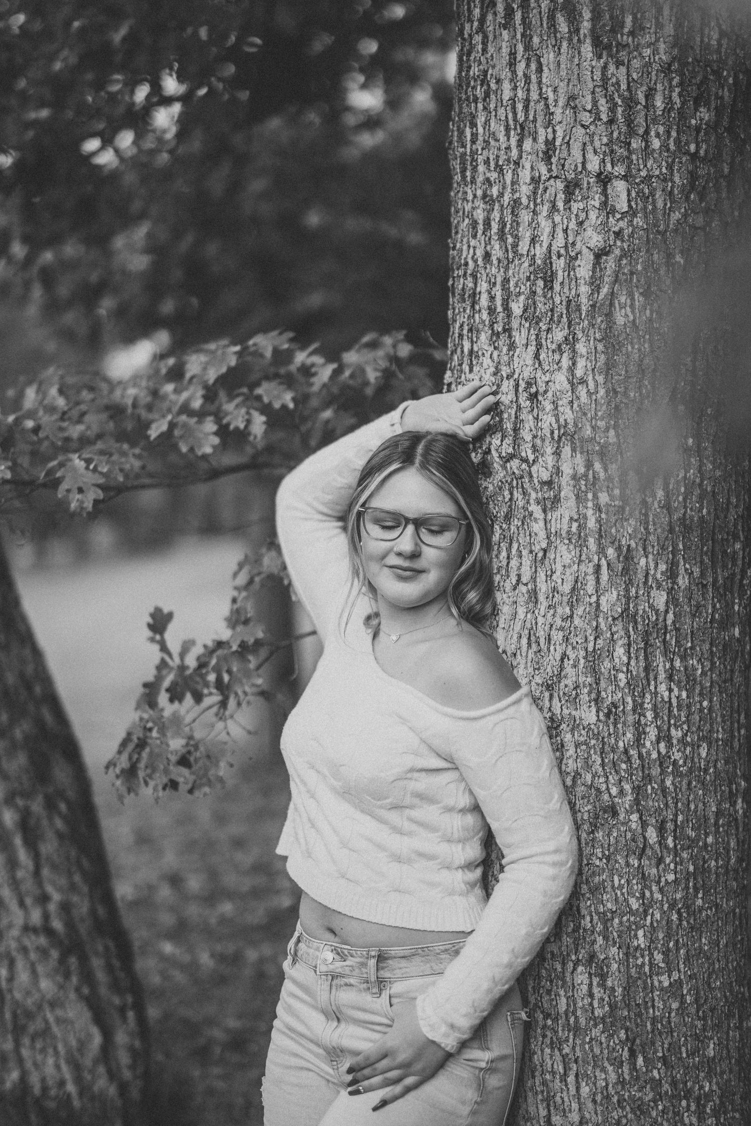 Black and white photos show a person in a white sweater posing playfully against a tree trunk in a natural outdoor setting.