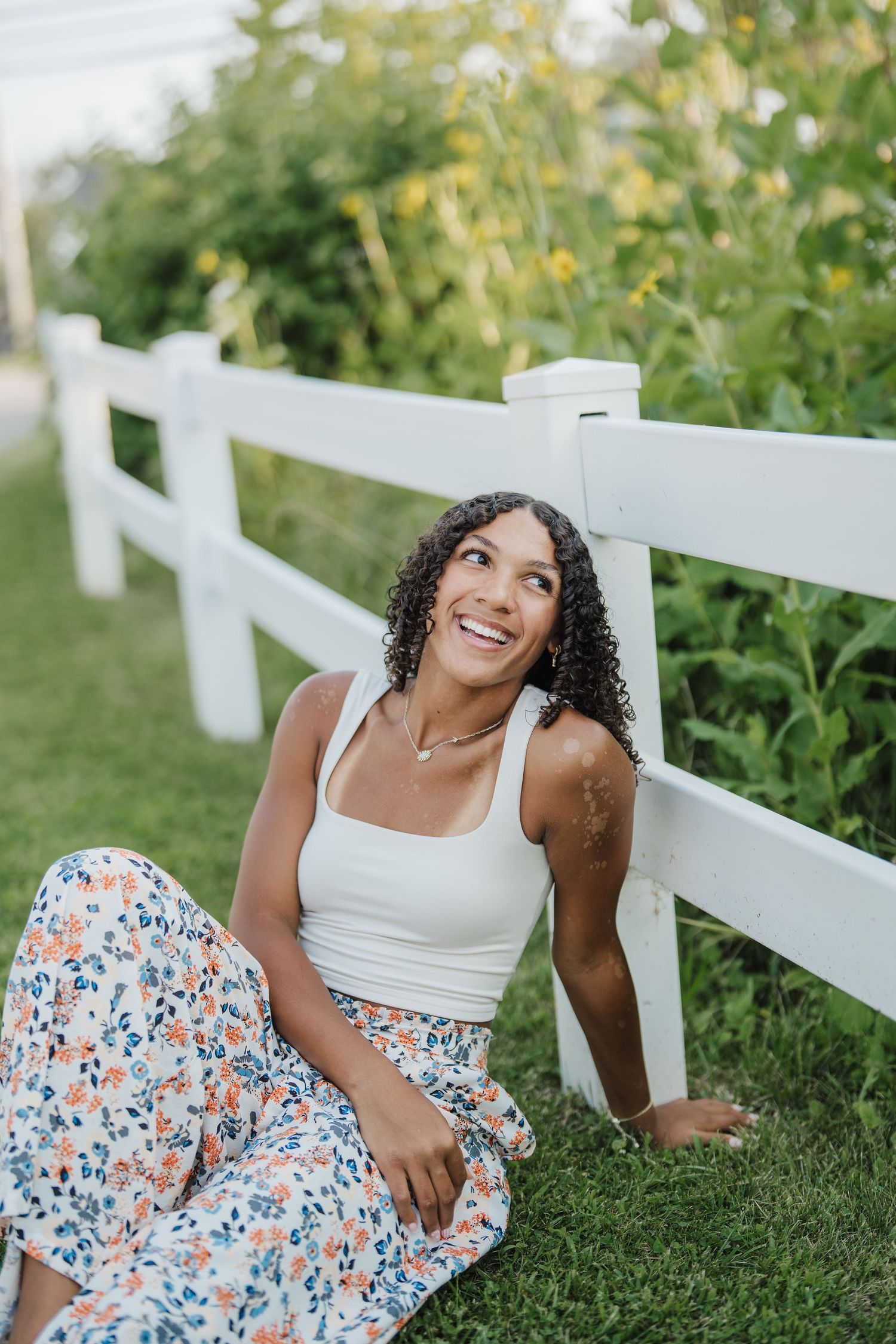 Relaxed outdoor portraits by a white picket fence featuring a floral dress and white tank top.