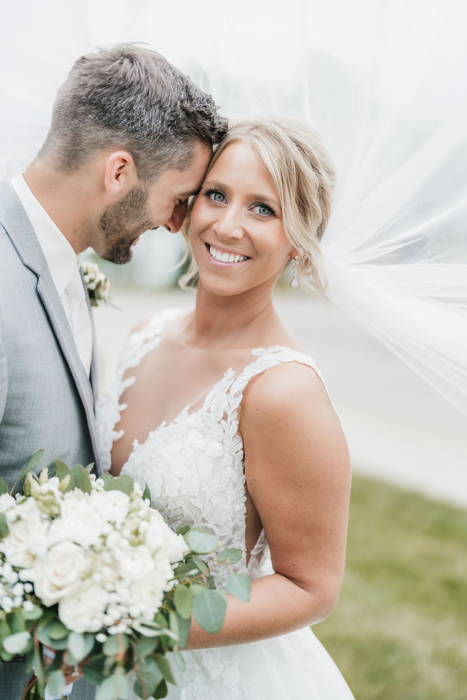 Intimate wedding portrait of newlyweds sharing a tender moment with white veil flowing.