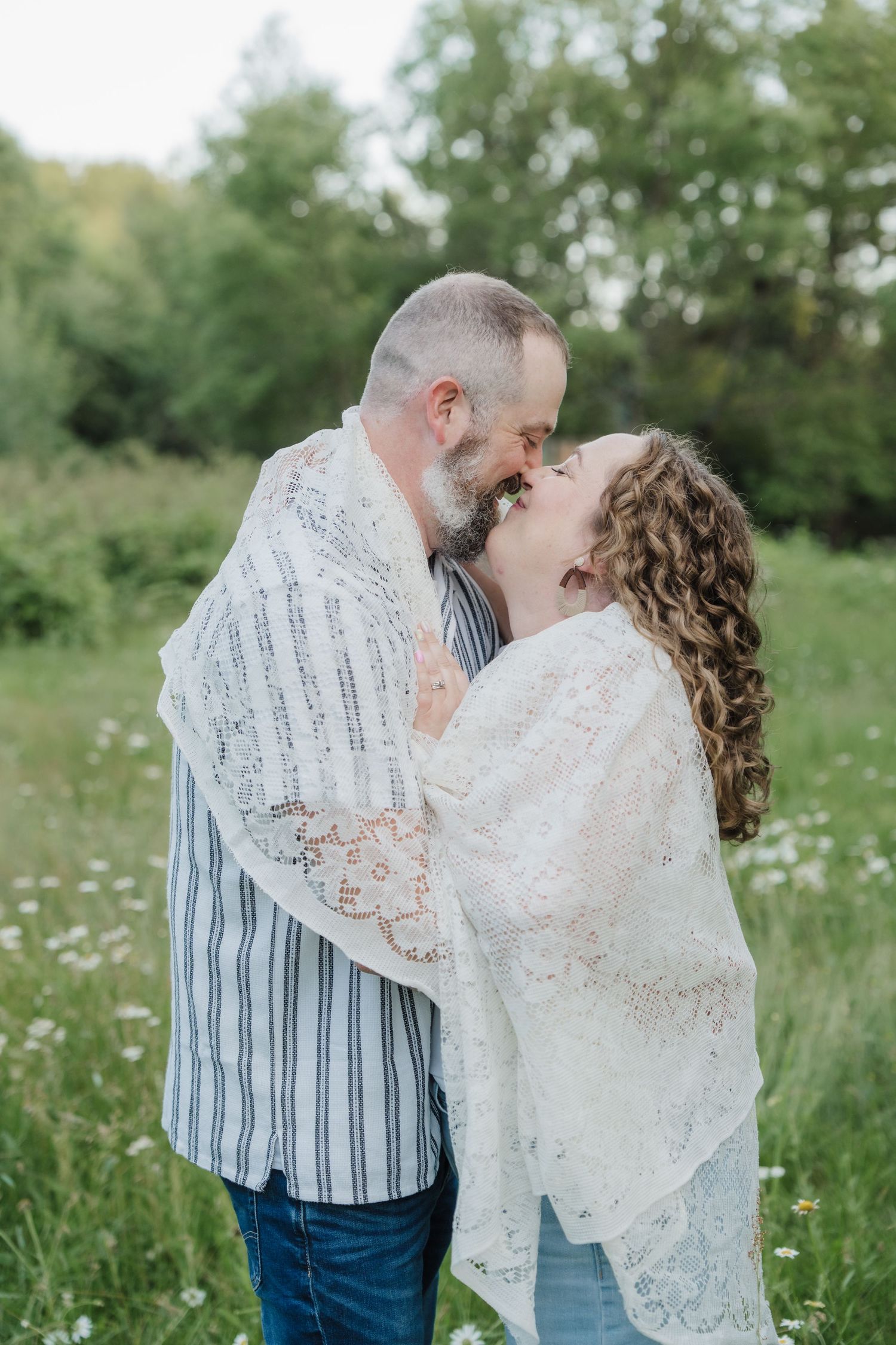 A happy couple shares a romantic almost-kiss while wrapped in lace in a blooming meadow.