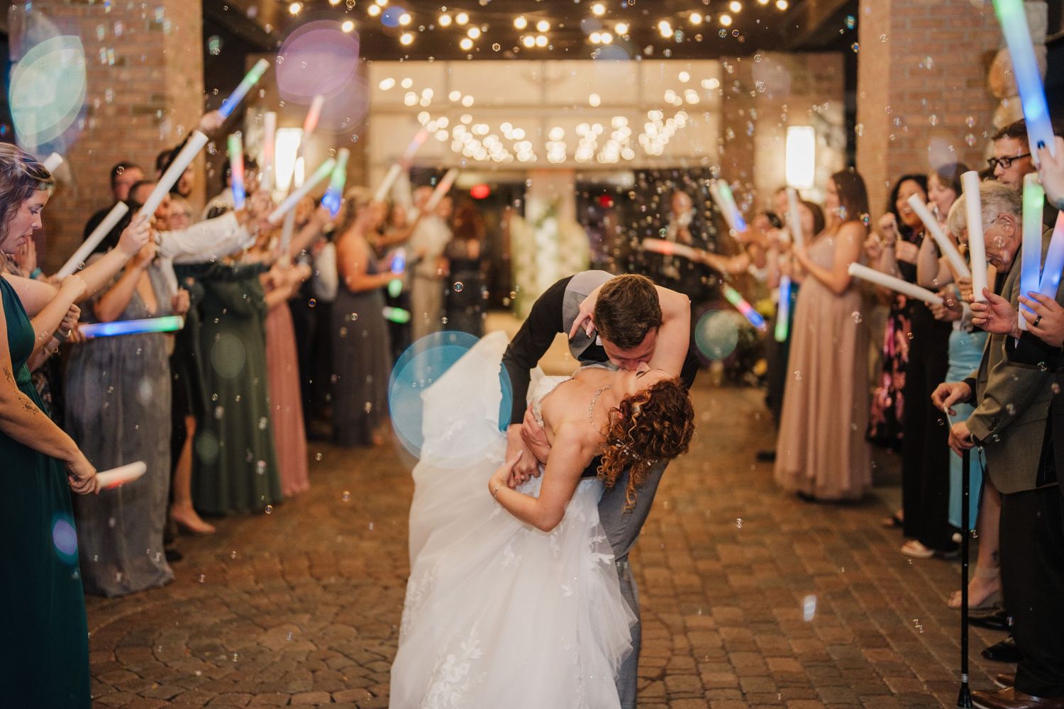 Wedding couple's first dance surrounded by guests with sparklers in a rustic indoor venue.
