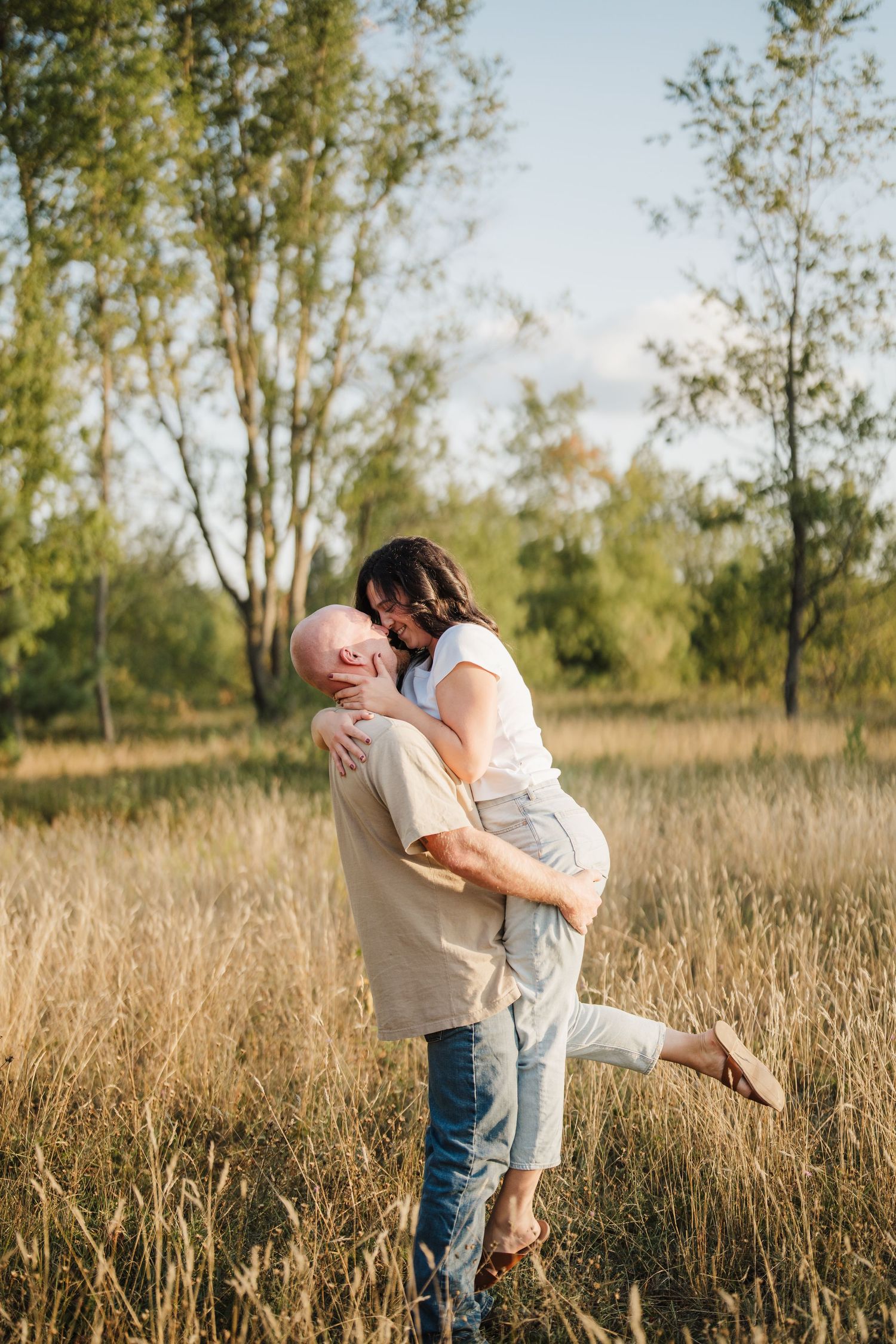 A romantic couple embraces in a sun-lit field of tall grass during a golden hour photoshoot.