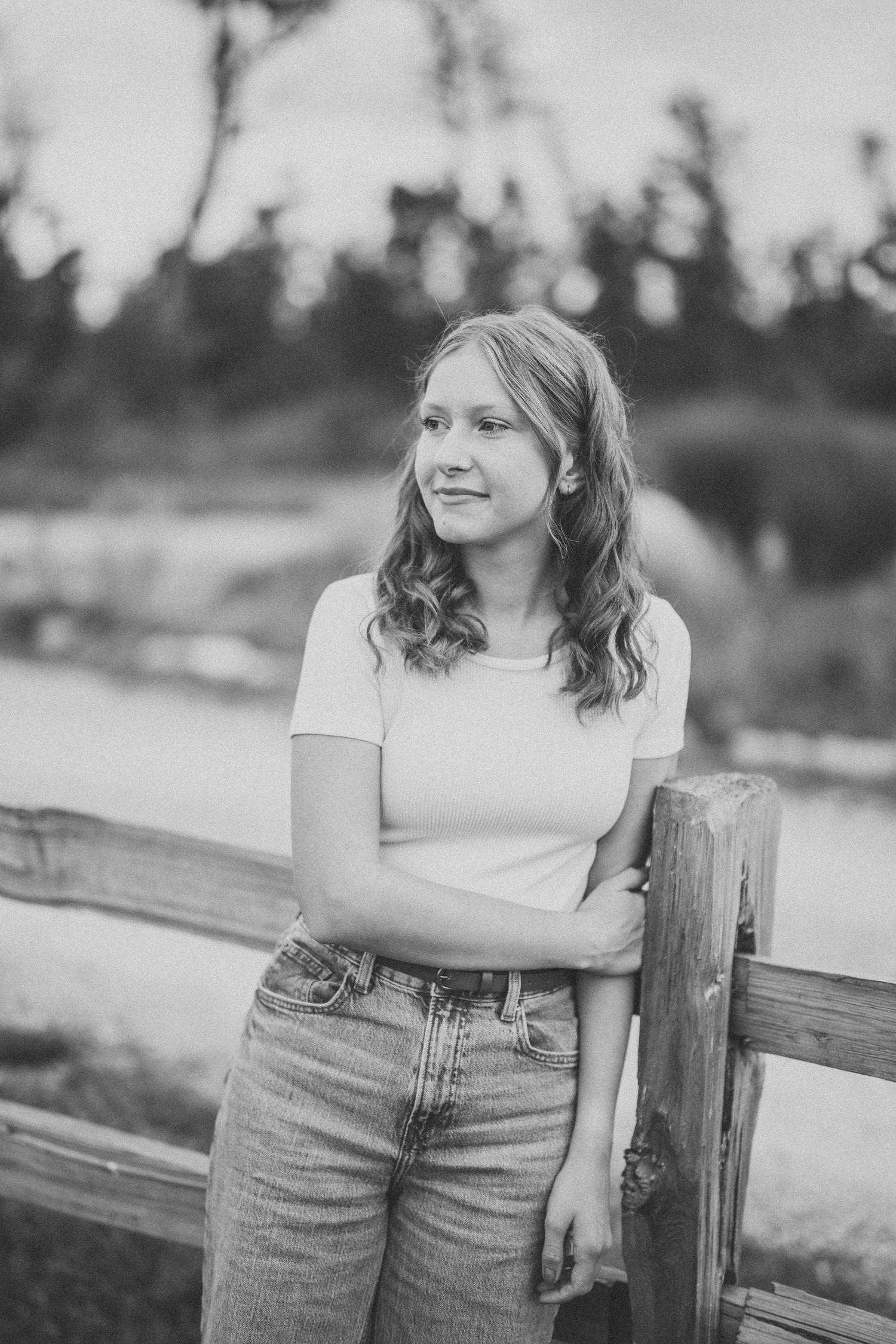 Black and white portrait series showing a casual pose against a wooden fence in jeans and a light colored top.