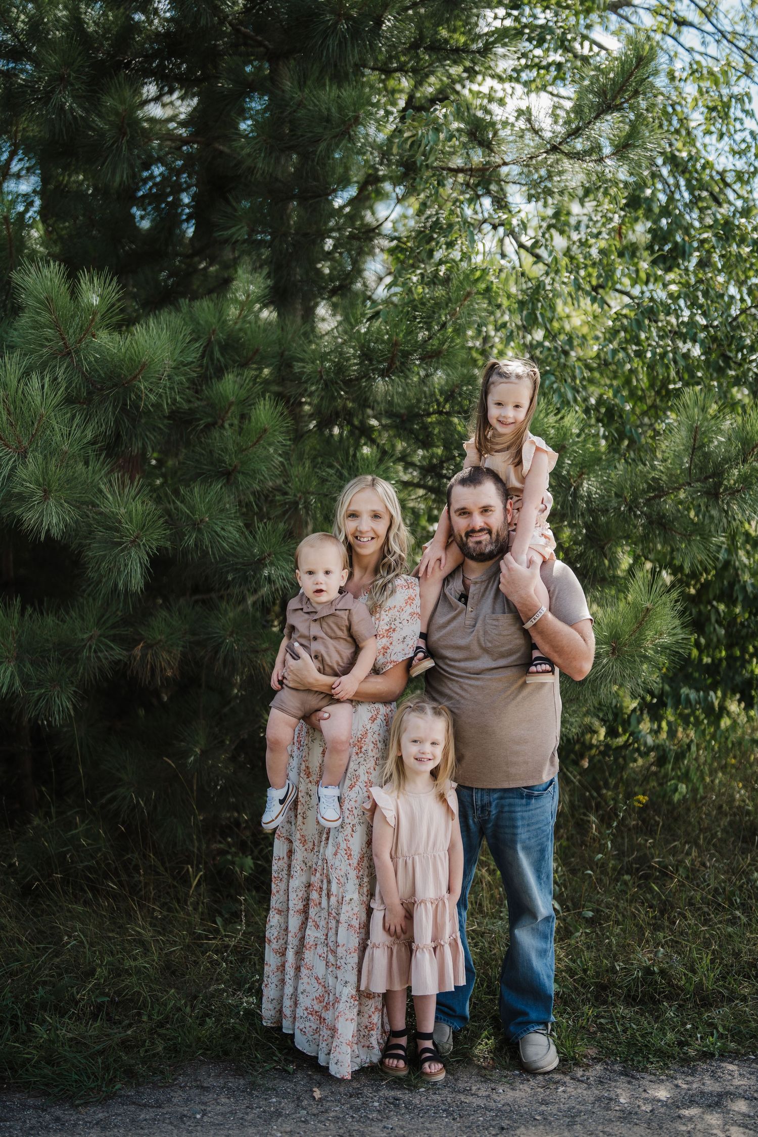 A family poses together outdoors against a backdrop of green trees and foliage in coordinating outfits.