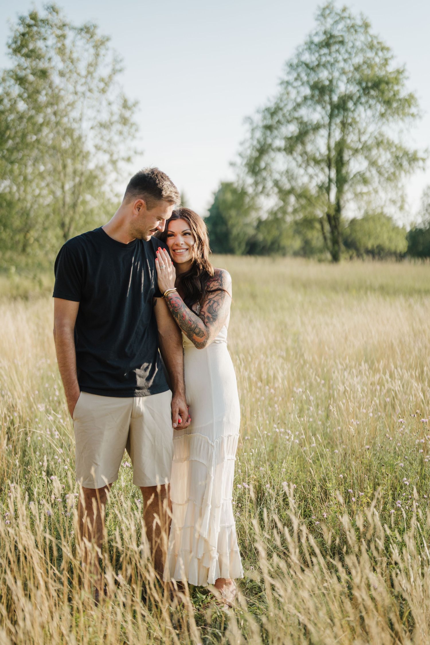 A couple shares an intimate moment while standing together in a sunlit meadow of tall grass.