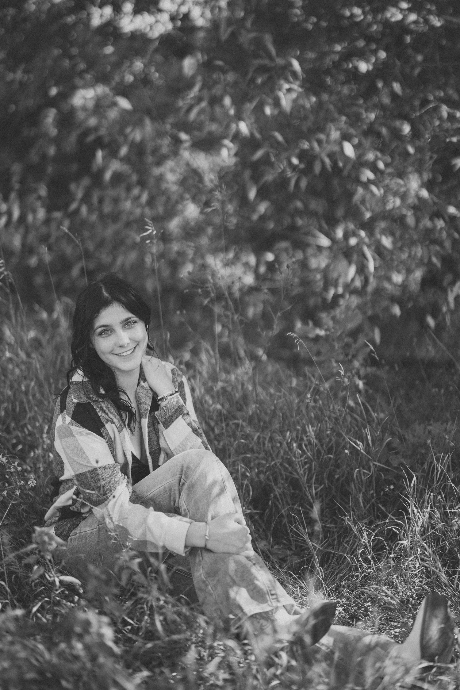 Black and white photo of someone sitting in tall grass with a dreamy, natural backdrop.