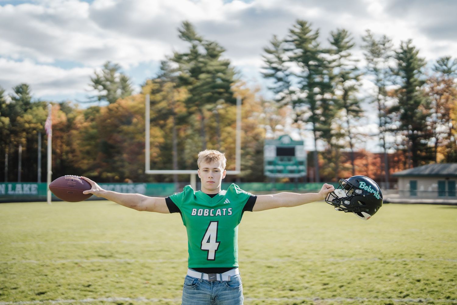 Football player poses with ball on green sports field during autumn season.