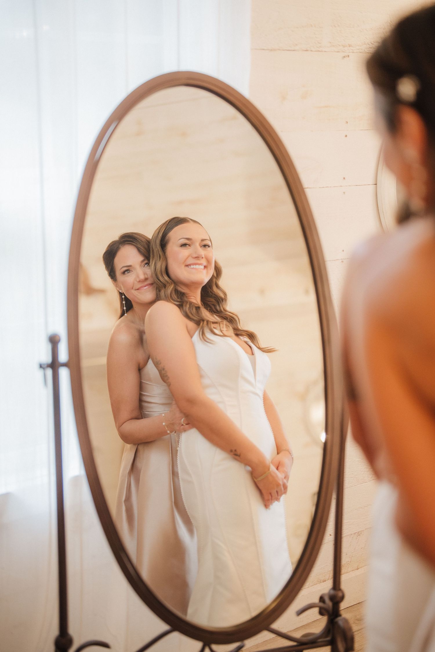 Bride admires her reflection in an oval mirror during wedding preparations.