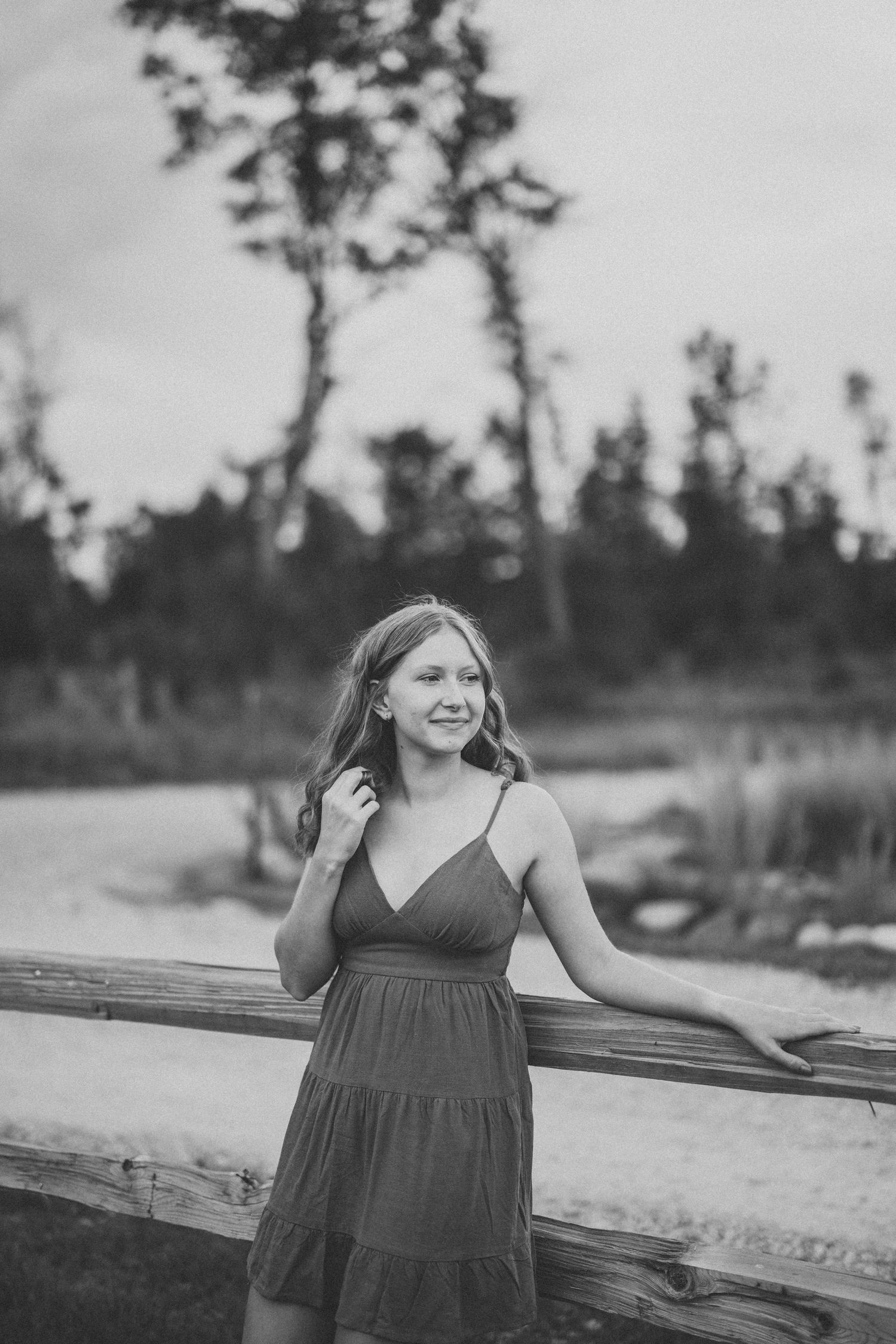A black and white outdoor portrait shows a relaxed pose against a natural landscape with trees in the background.