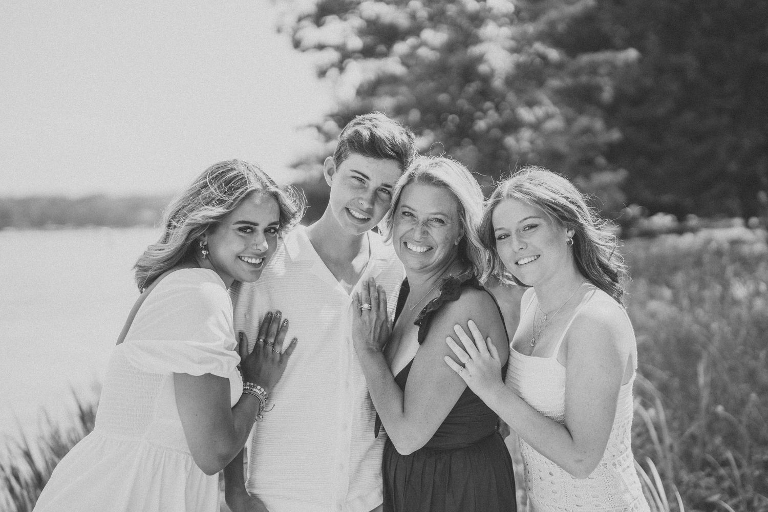 A group of people laughing and embracing together outdoors in a candid black and white photo.