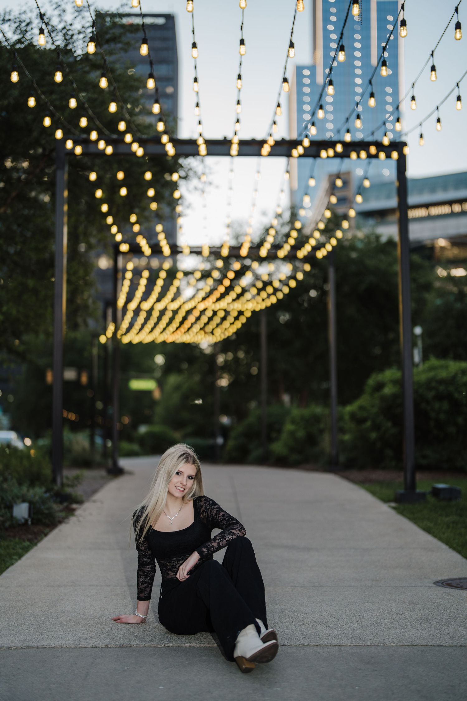 Artistic portrait session under illuminated string lights on a concrete walkway at dusk.