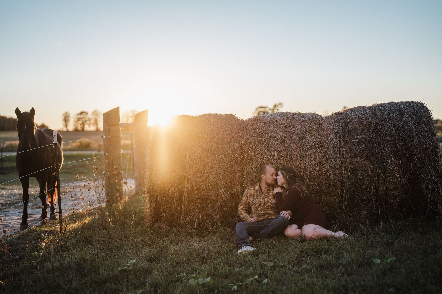 A series of silhouetted figures stand against a golden sunset in a grassy field creating a dreamy outdoor scene.