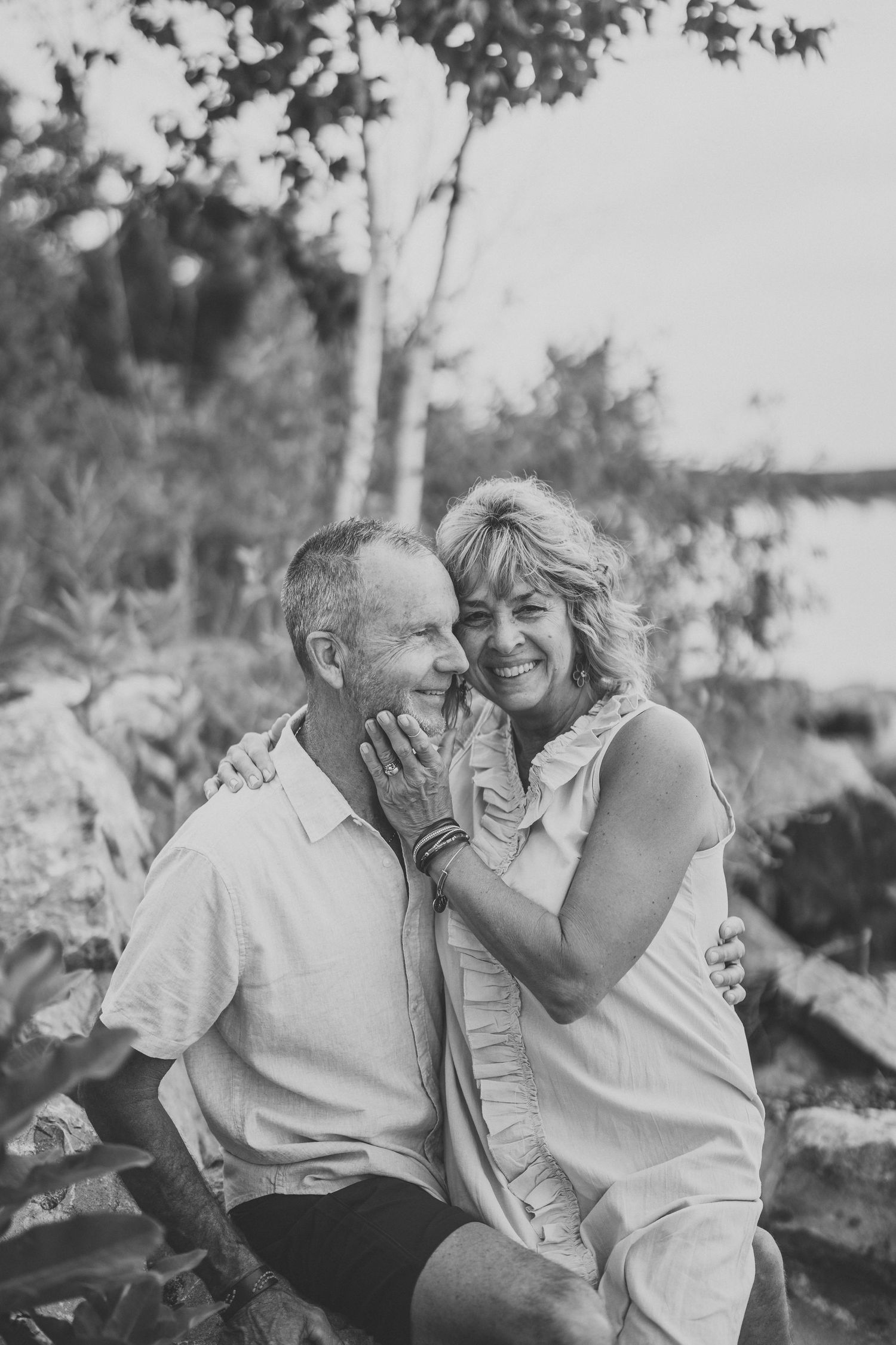 Black and white photo series showing a couple laughing and embracing outdoors in a natural setting.