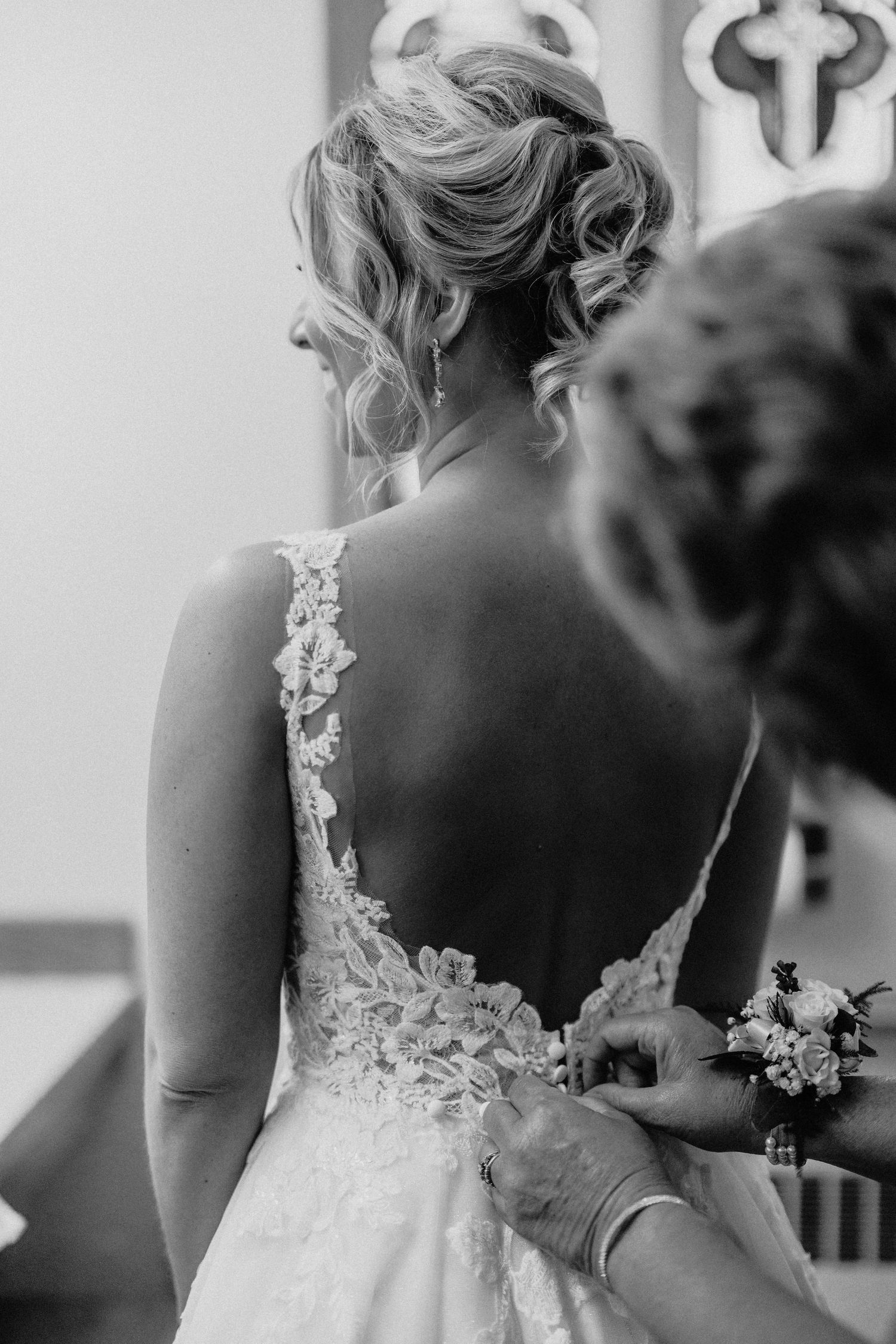 Black and white detail shot of bride's lace back wedding dress being buttoned.