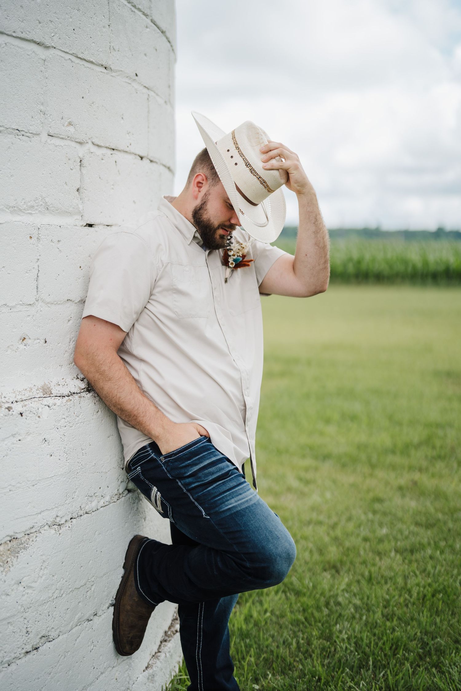Person in casual attire and cowboy hat leans against white wall in rustic setting.