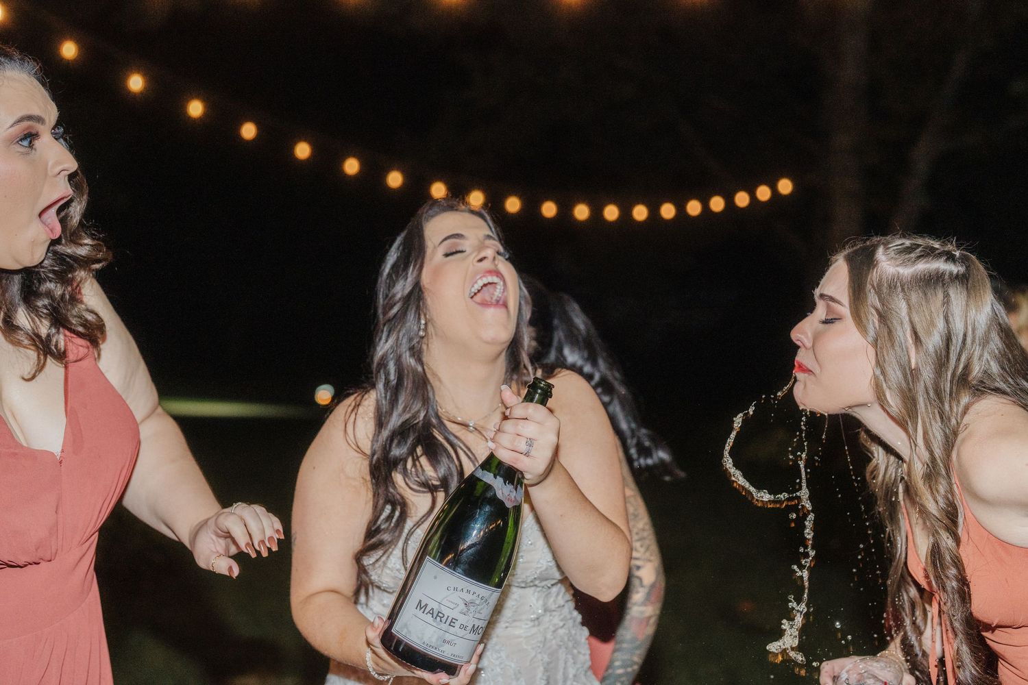 Wedding guests dancing and celebrating under warm string lights at night reception.